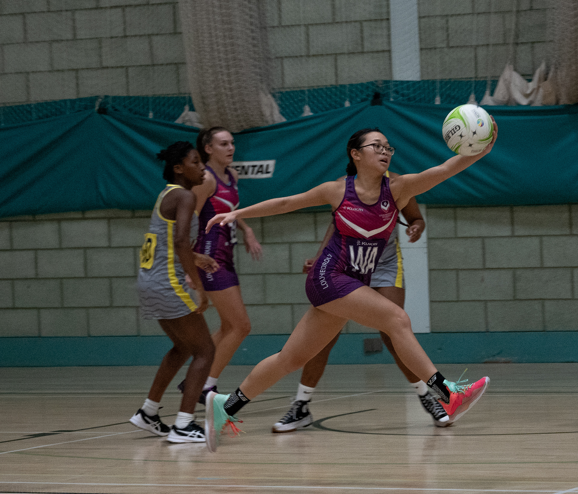 A young women jumping forward with a netball in her hand