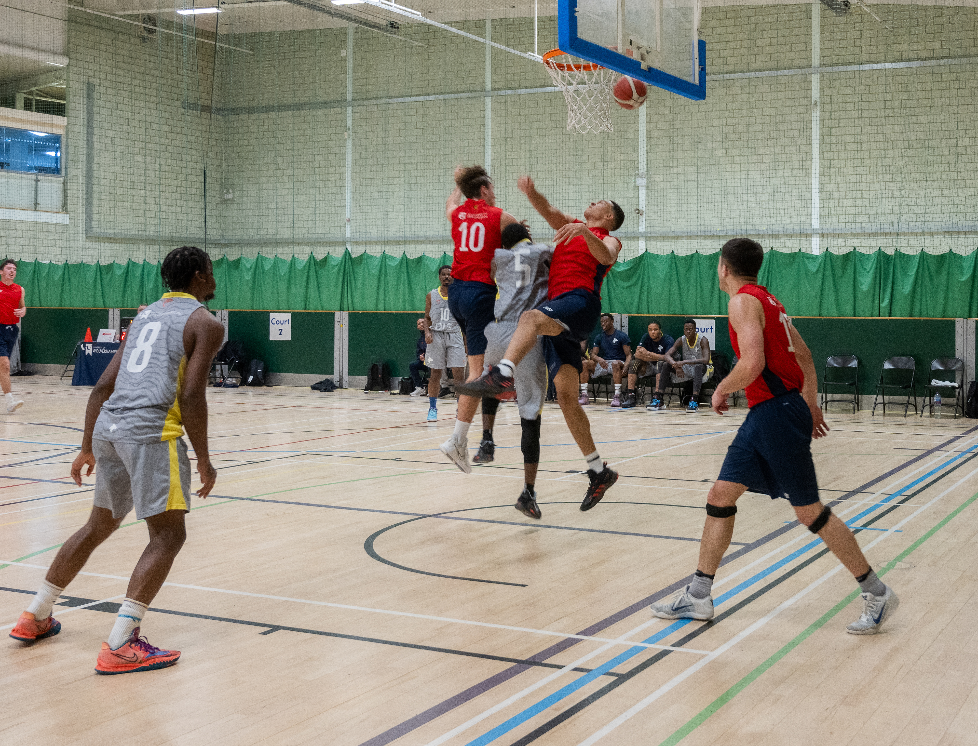 Three men jump up towards a basket ball hoop