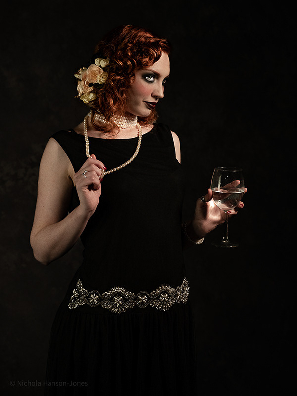 Roaring 20's shoot - female model dressed in a black dress holding a glass of wine