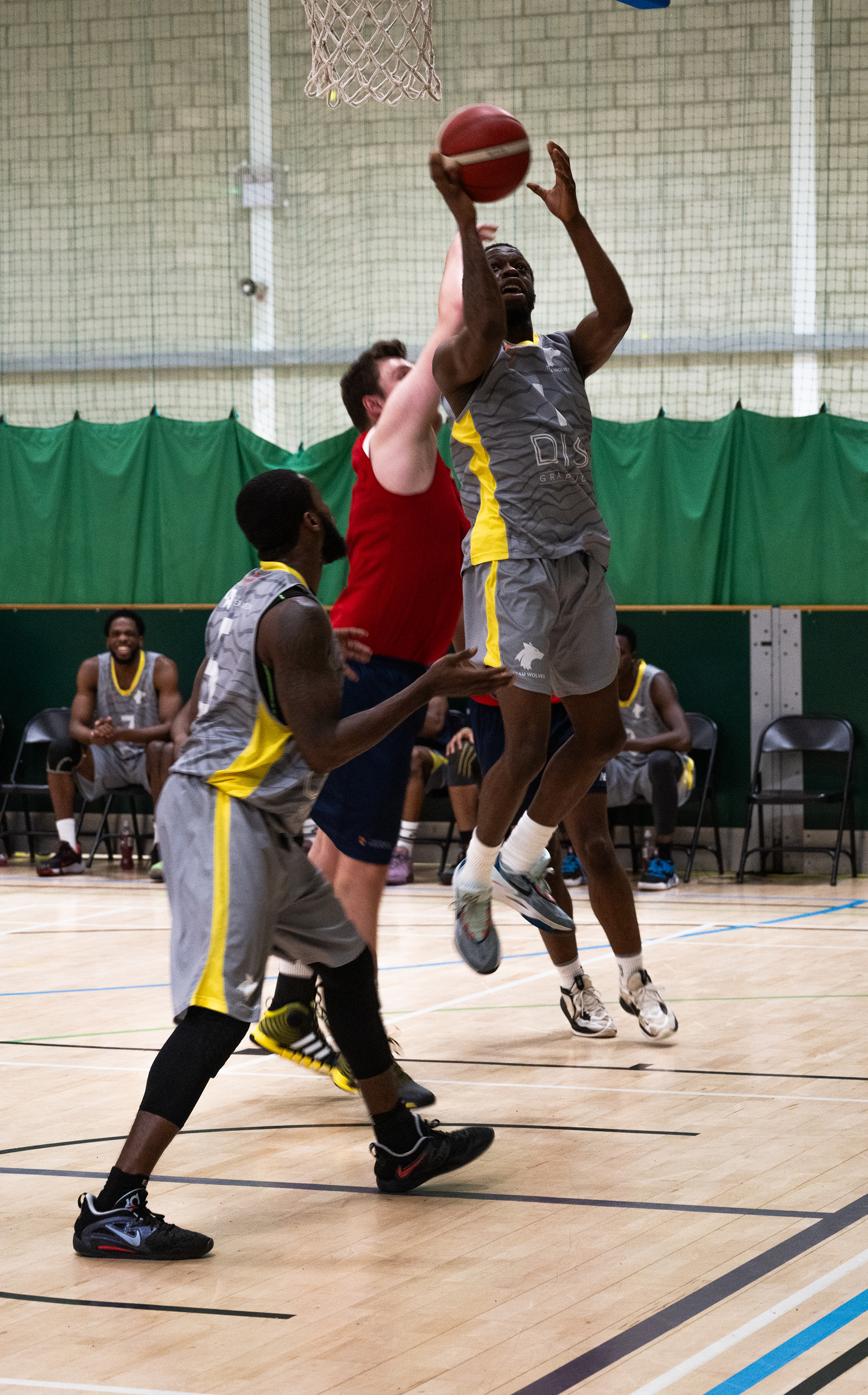 Two basket ball payers try to stop a third from scoring