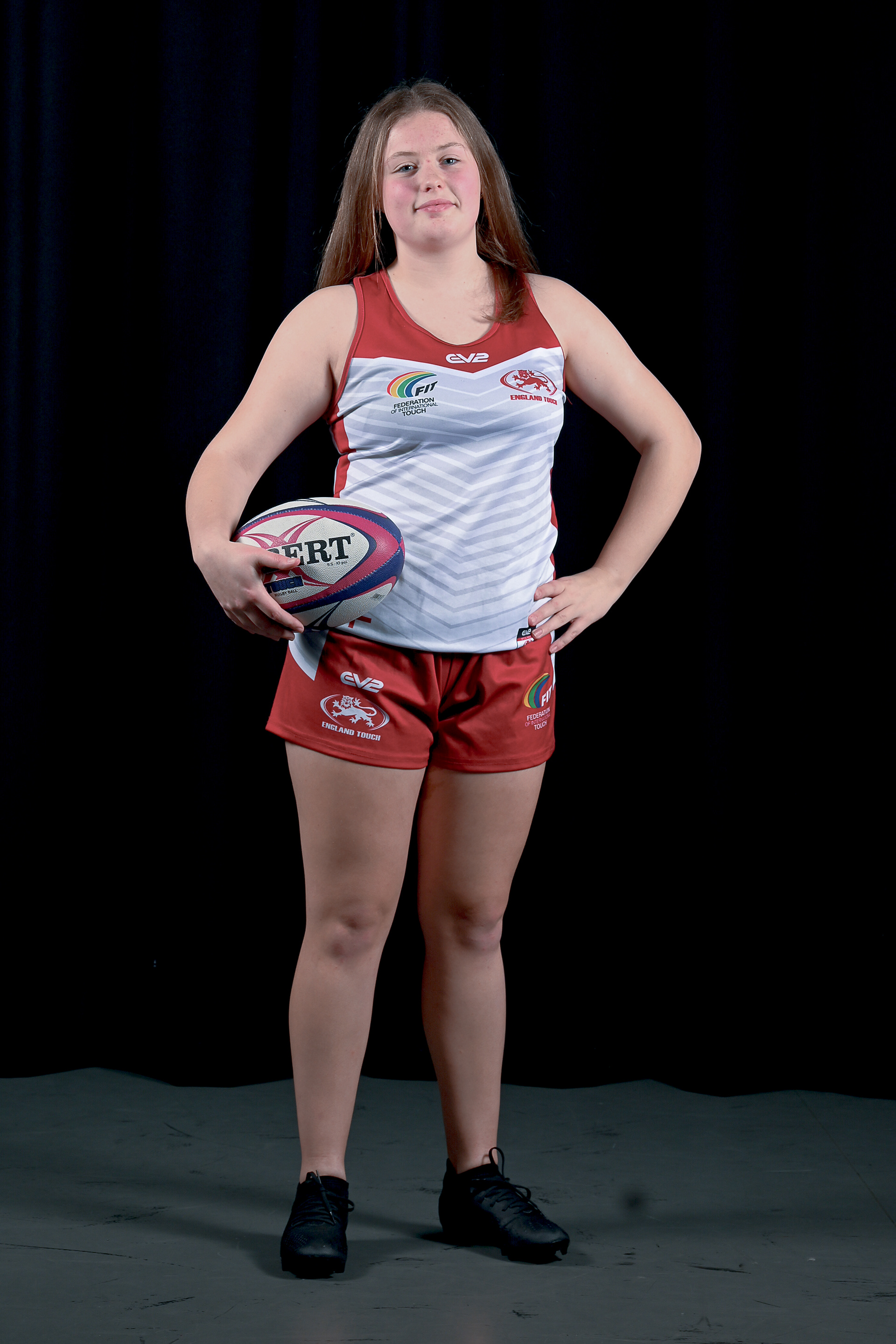 A young women in shorts and a vest hold a rugby ball