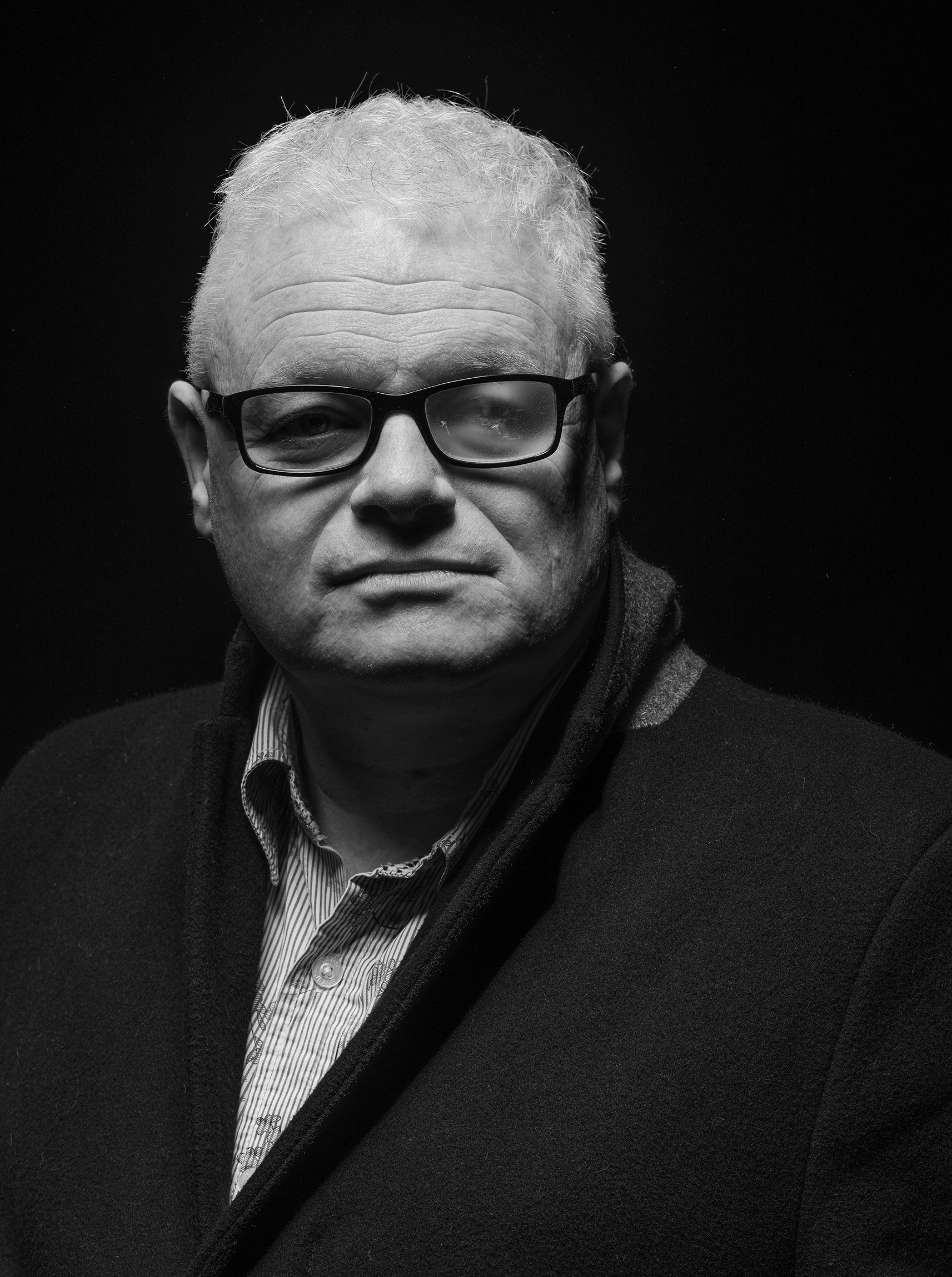 A image of a man, wearing glasses he is looking at the camera. You can see that theleft hand lens of his glasses is blurred.