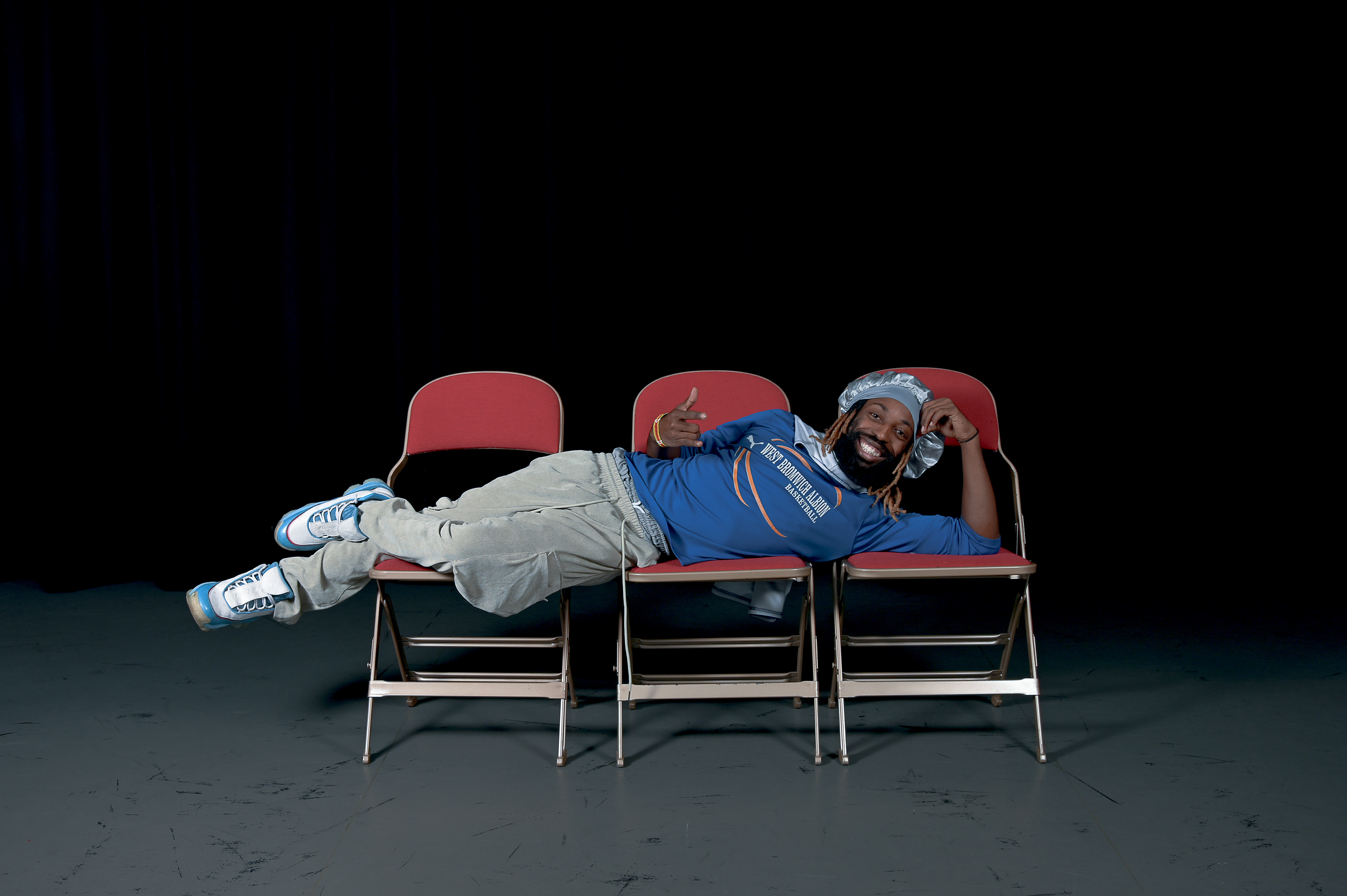 A man wearing sports attire, he is lay across three red chairs