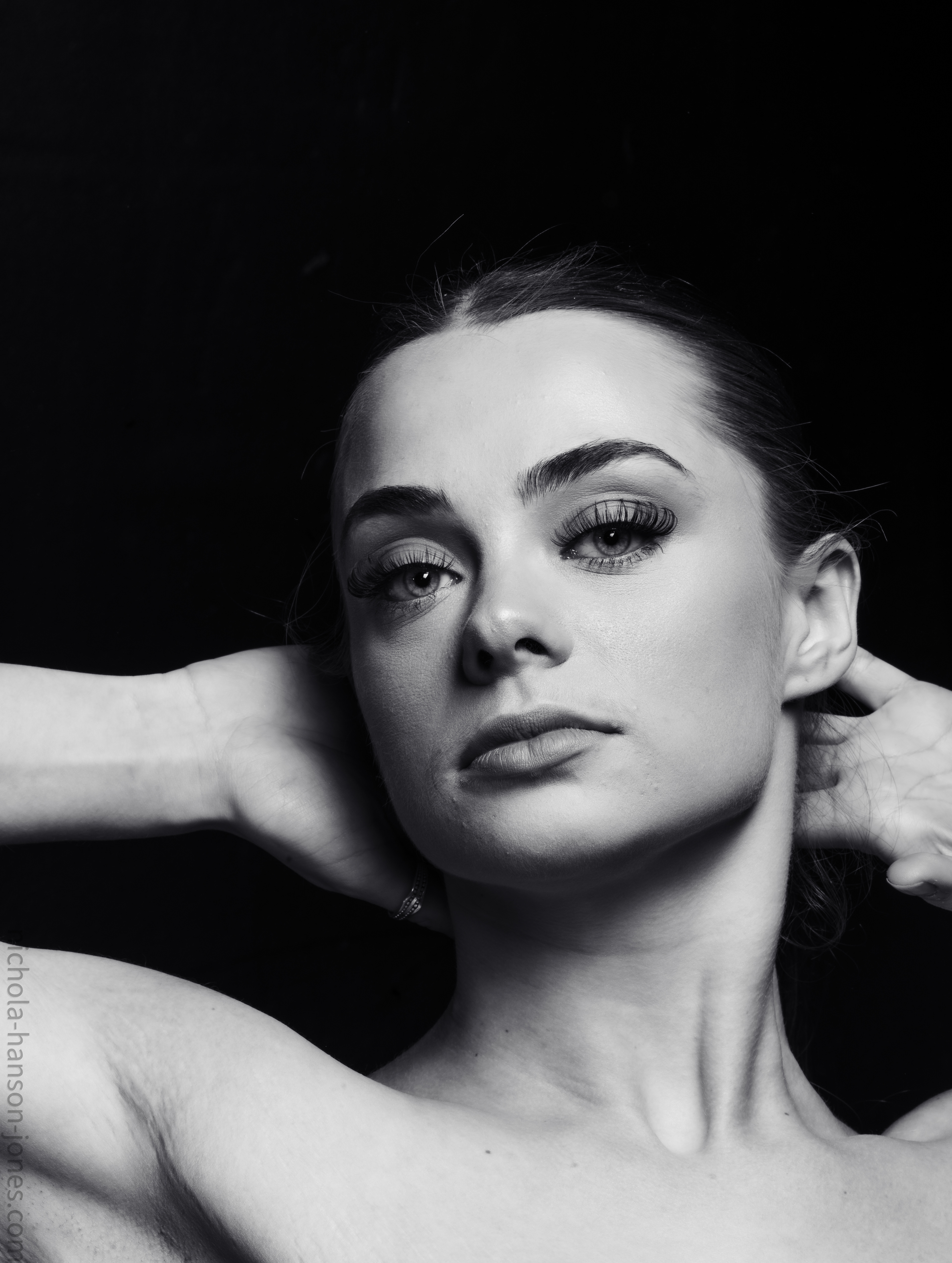 Courtney-Portfolio Shoot  A young woman looks at the camera she has her arms raised behind her head.