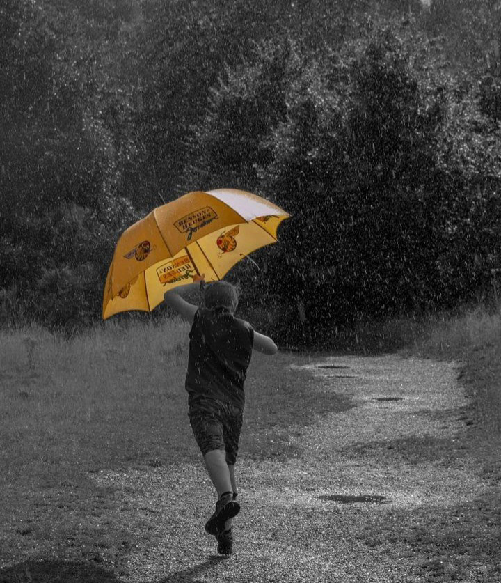 Sunshine and Showers shoot - A young boy running away from the camera he is carring a big yellow umbrella 