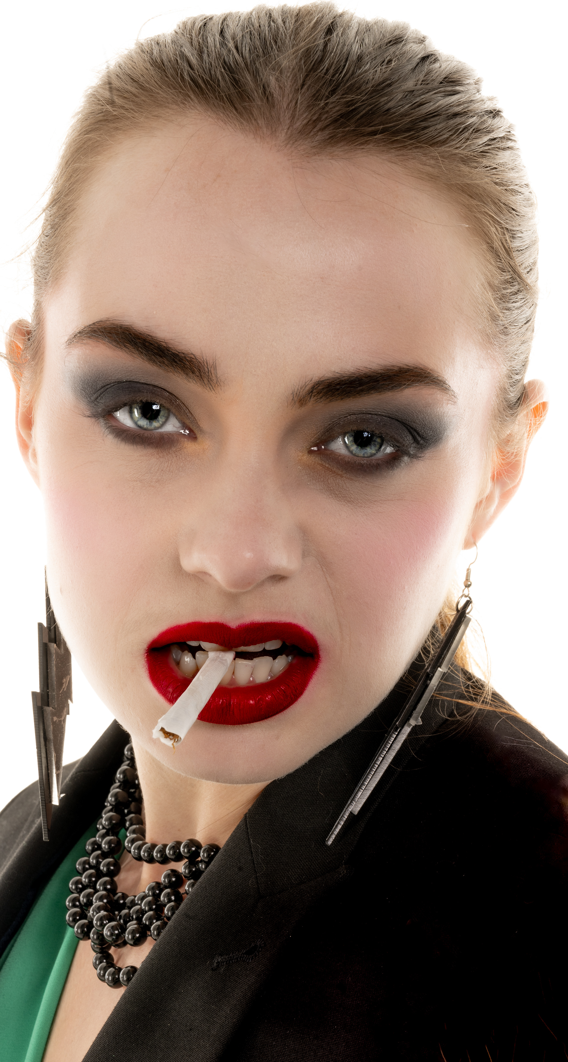 Eighties Vamp - Portfolio shoot  - A young woman has her hair scraped back from her face, she has bright red lipstick on her lips are parted and between her teeth she holds an unlit cigarette 