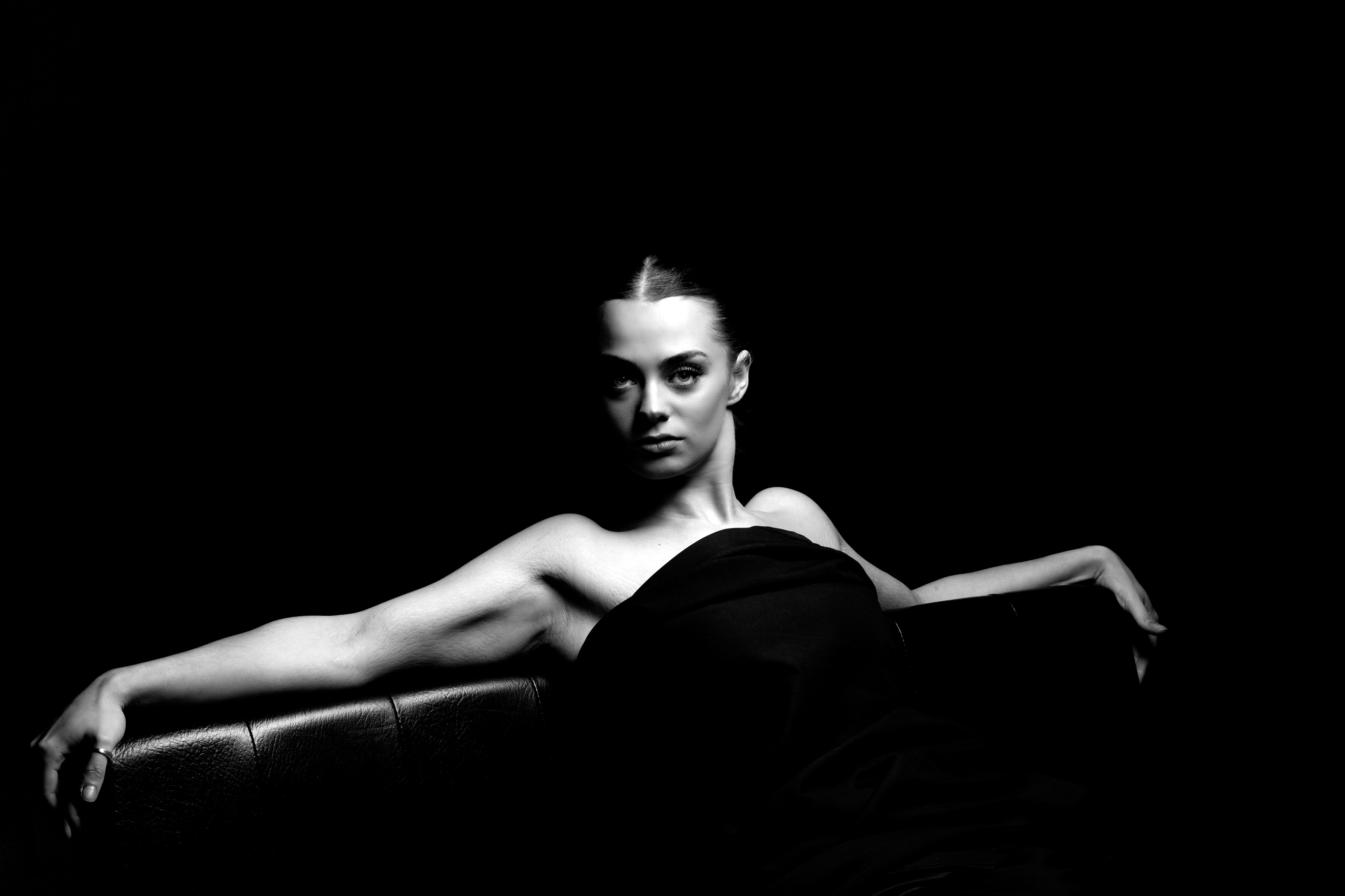 Courtney-Portfolio Shoot  - a young woman reclining against the back of a sofa, her arms are draped across the back of the sofa and she is looking straight at the camera. 