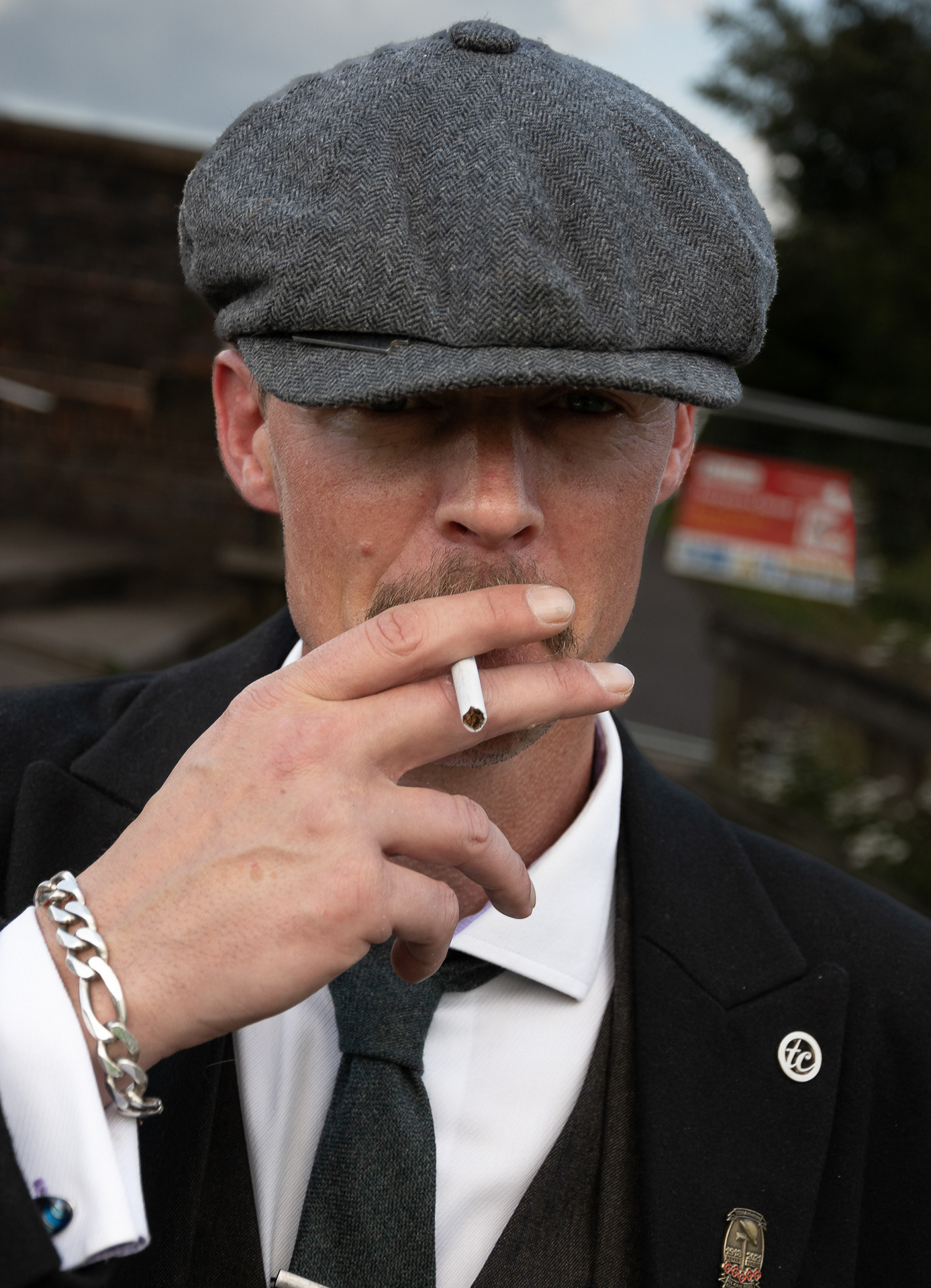 Peaky Shoot A man wearing a suit and flat cap looks at the camera while he smokes a cigarette