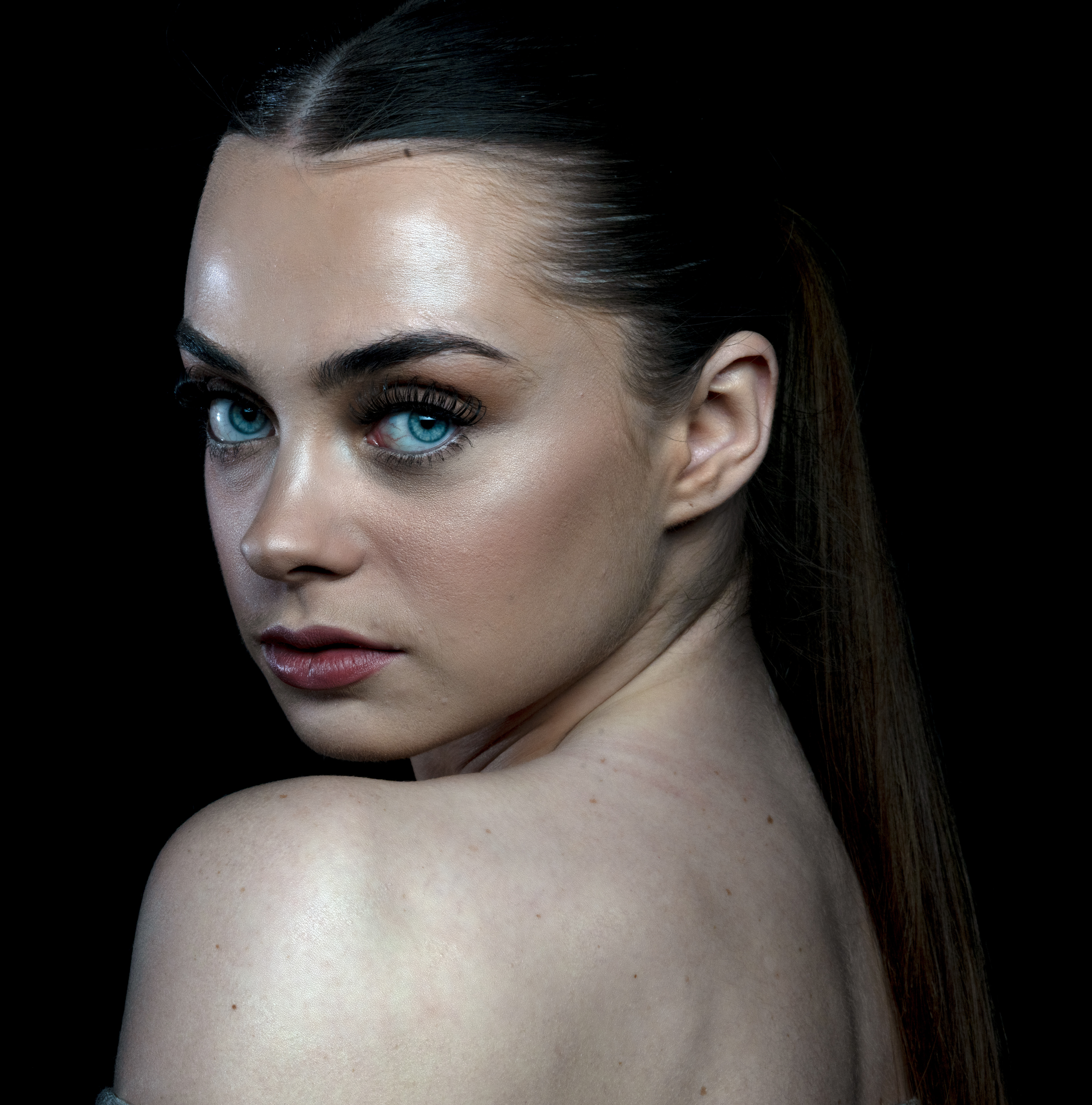 Courtney- Portfolio Shoot  A young woman with bare shoulders looks over her left shoulder at the camera 