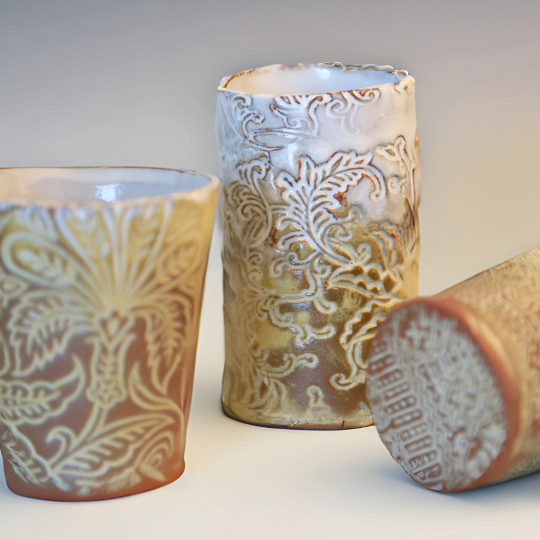 3 handmade ceramic mugs with de-bossed floral patterns in shades of white, tan and gold.