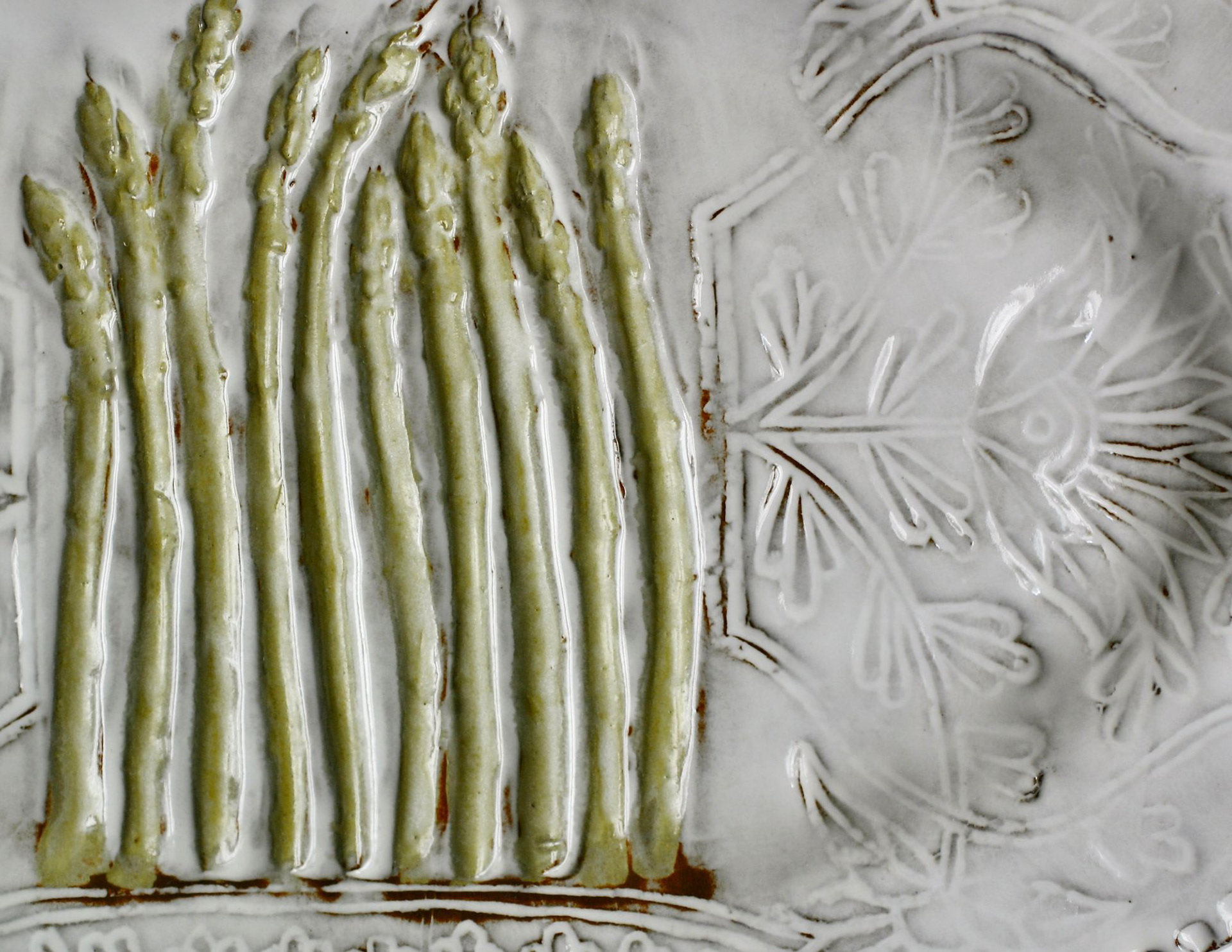 Close-up of a handmade ceramic platter with raised asparagus details over a de-bossed delicate white floral pattern.