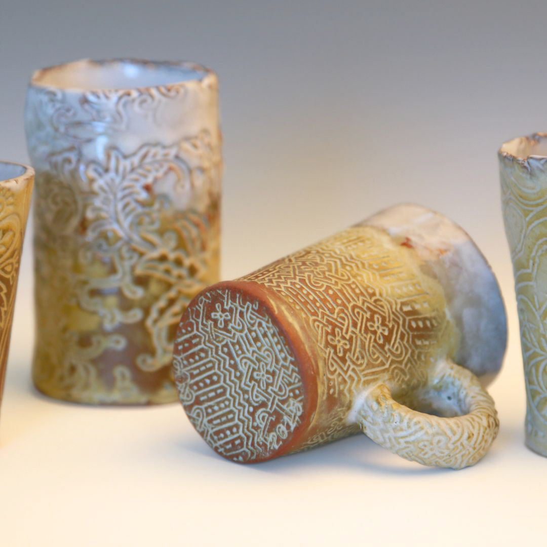 three handmade ceramic mugs with de-bossed floral patterns in shades of white, tan and gold.