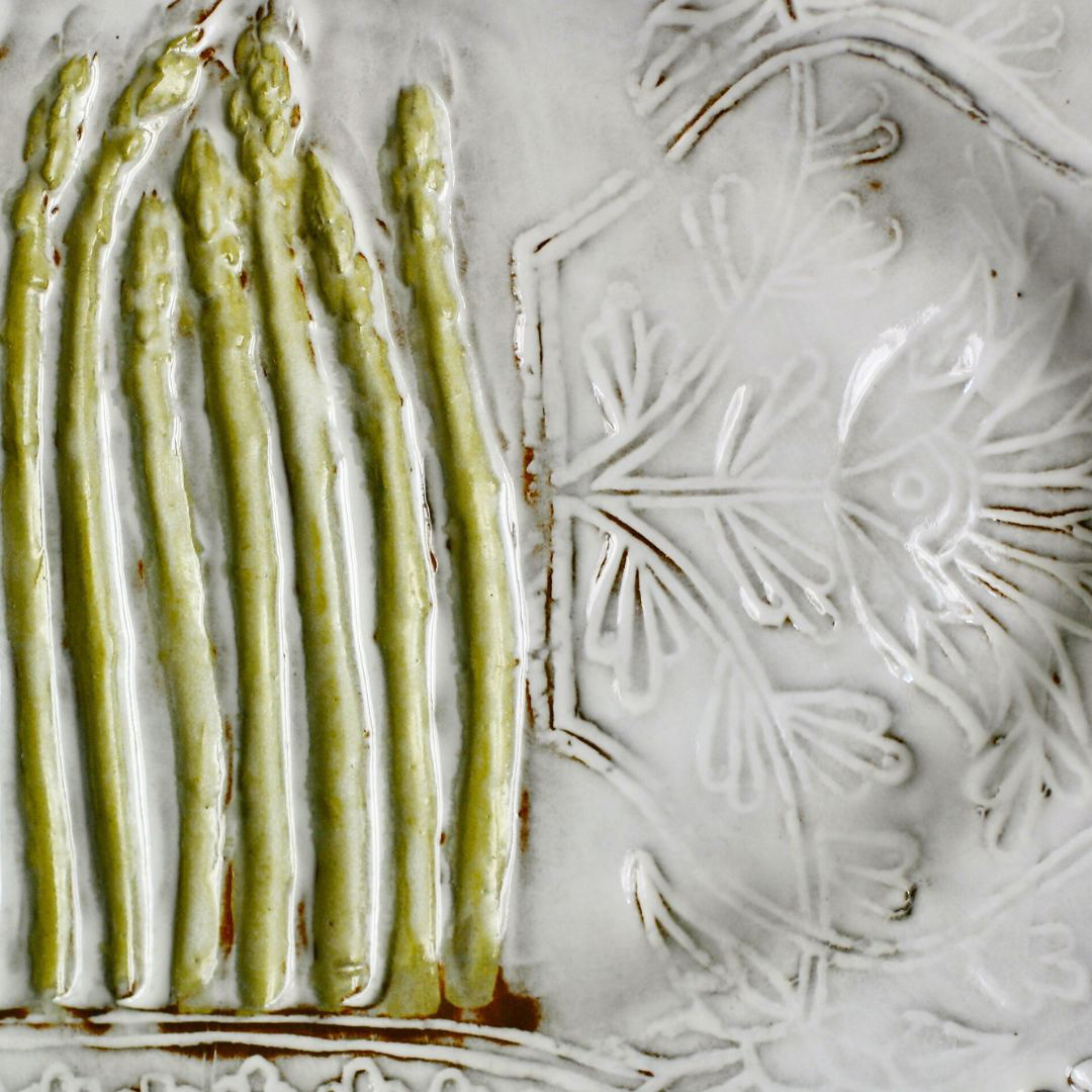 Close-up of a handmade ceramic platter with raised asparagus details over a de-bossed delicate white floral pattern.