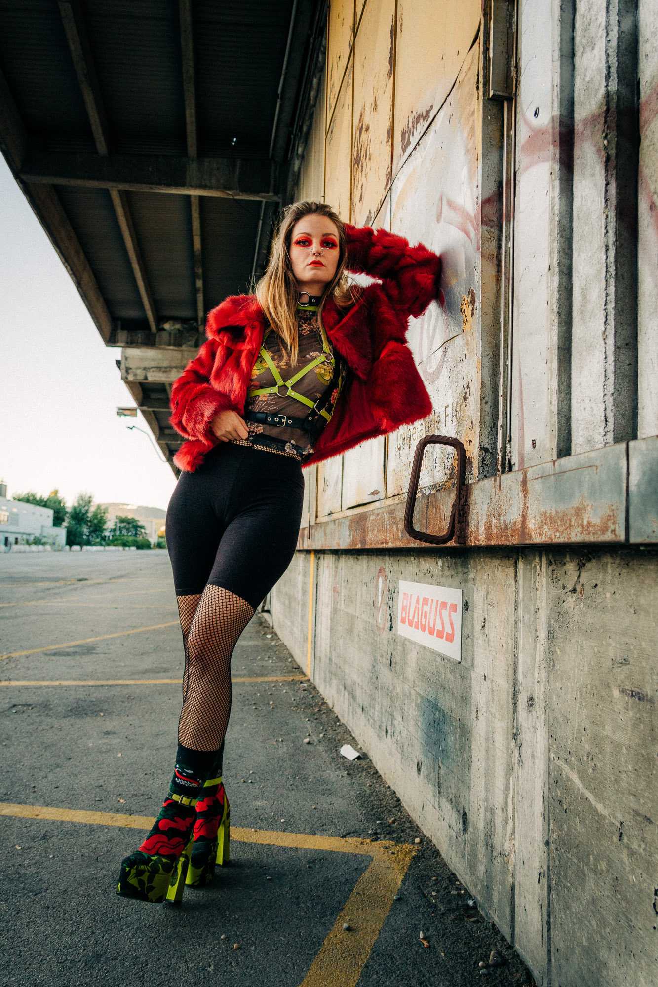 Portrait of a young woman in an extravagant outfit leaning against a wall at an industrial site