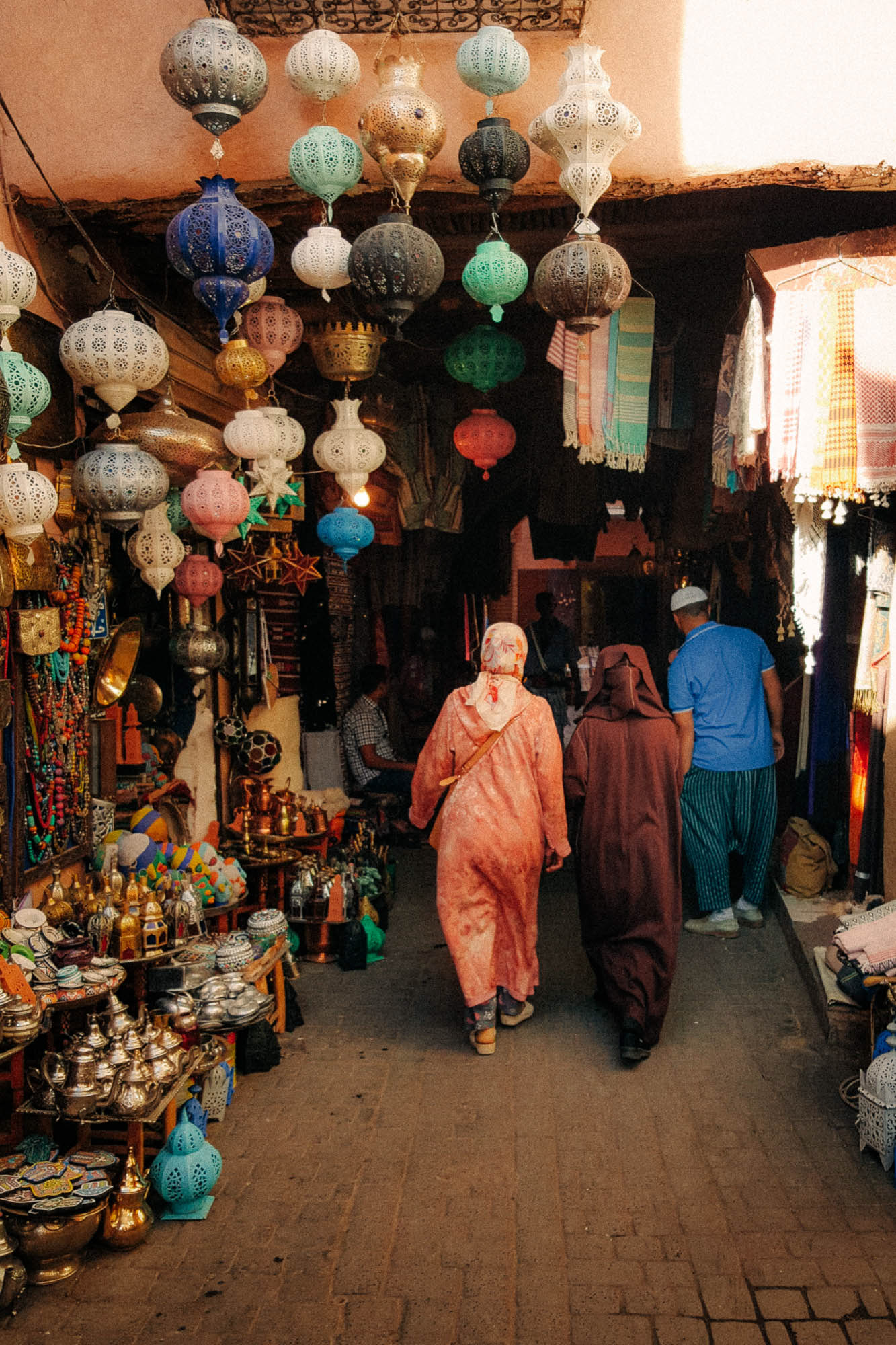 Street photo taken in the souks of Marrakech showing poeple in traditional clothes walking by a stand selling