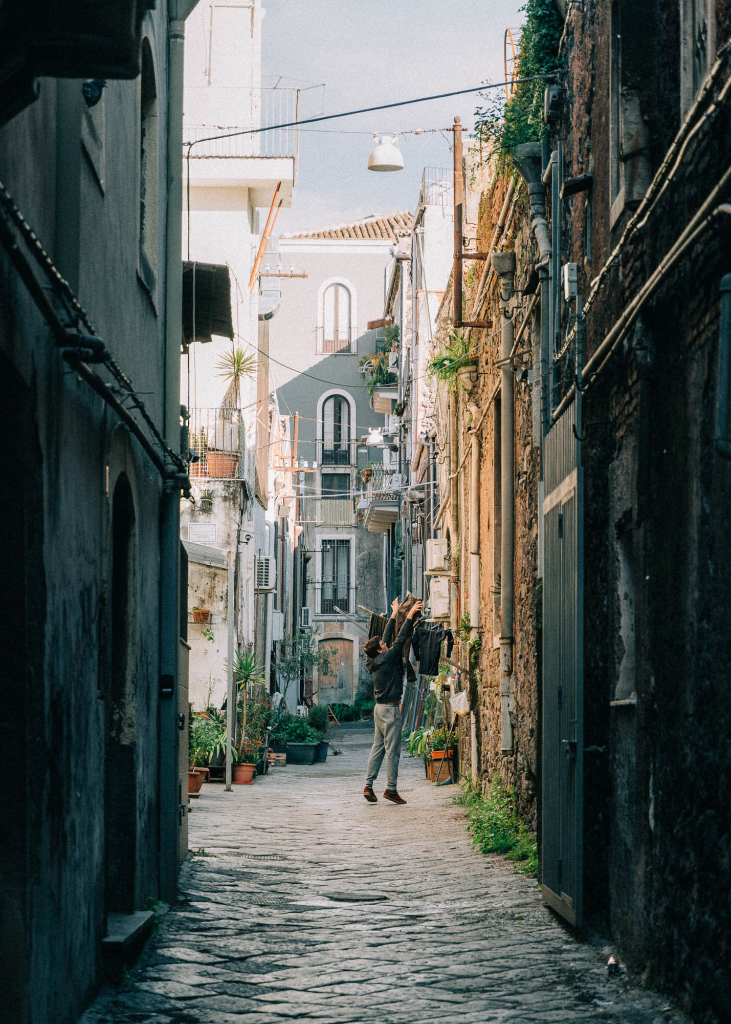 Street photography showing a man hanging up laundry in Catania