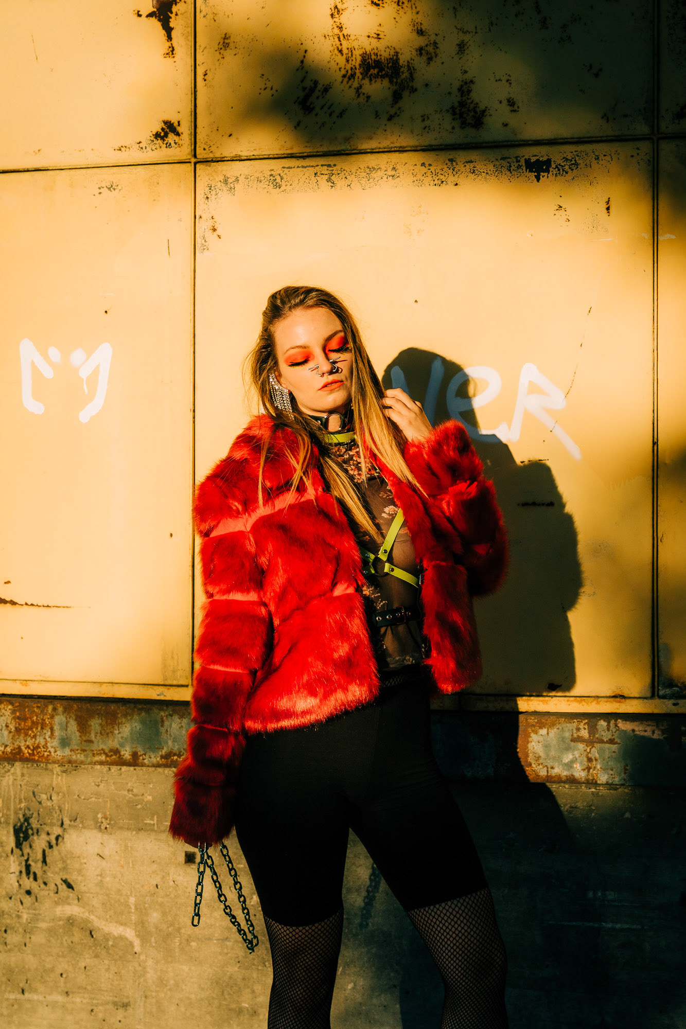A young woman with a red fur coat poses in the sunlight