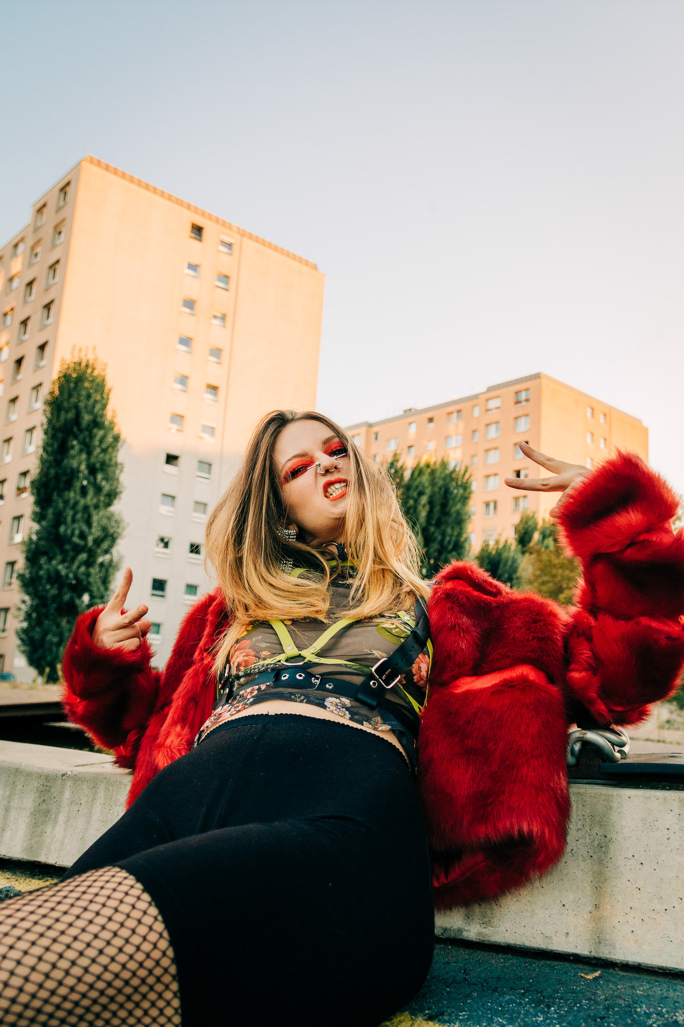 Low angle shot of a girl with red makeup, a red fur coat and a leather harness