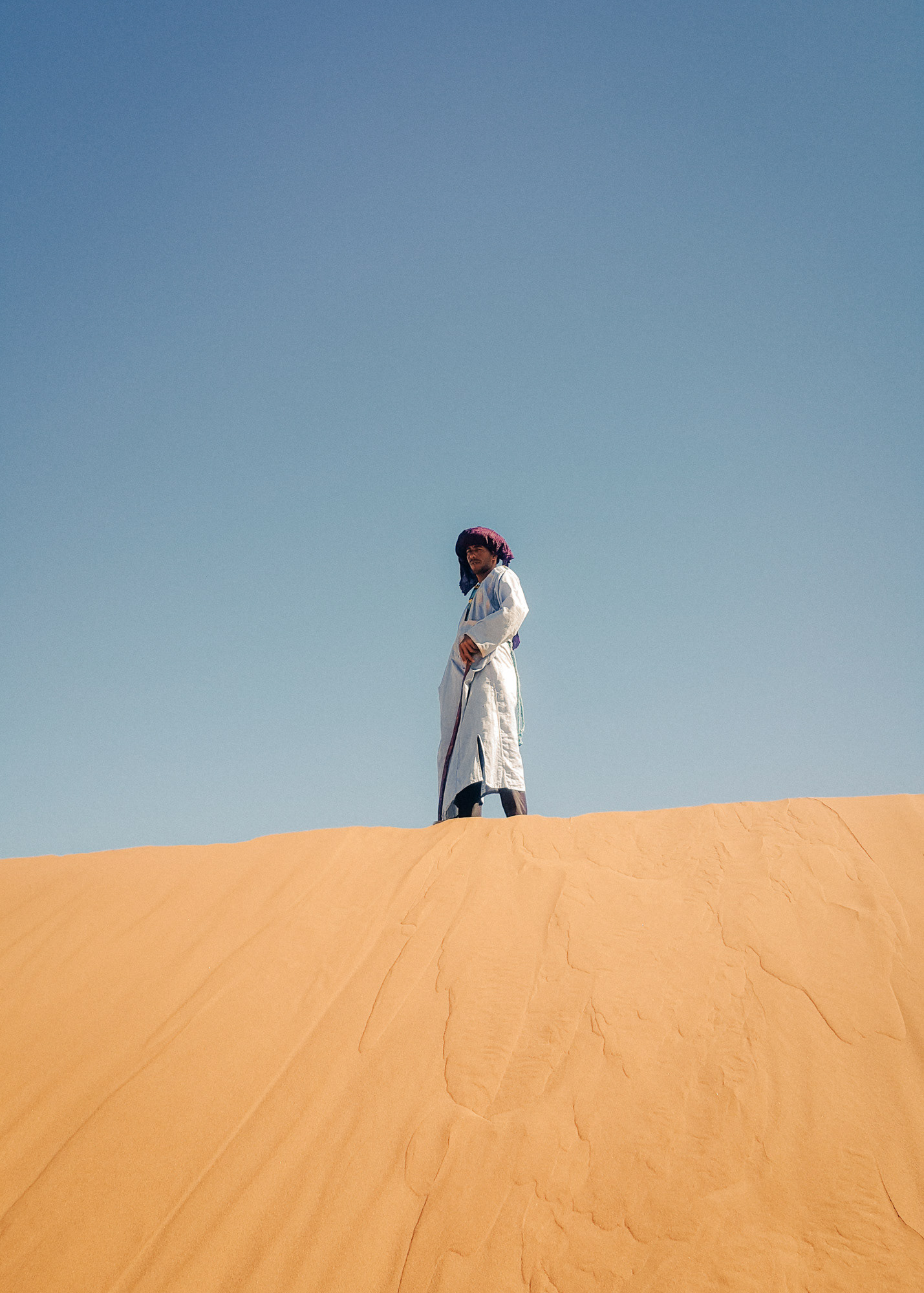 Portrait of a Berber man standing on a dune in the Sahara desert gazing into the distance