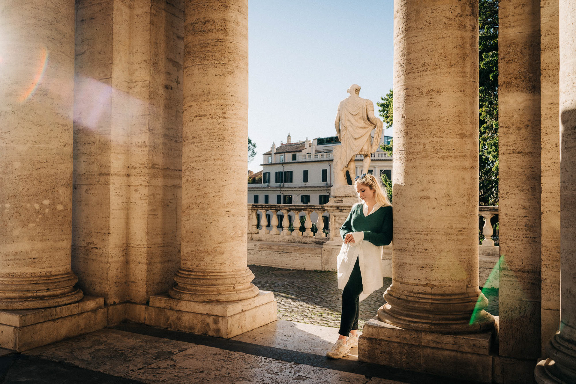 Portrait of a girl standing between large columns at Piazza del Campidoglio as the sun casts a lens flare