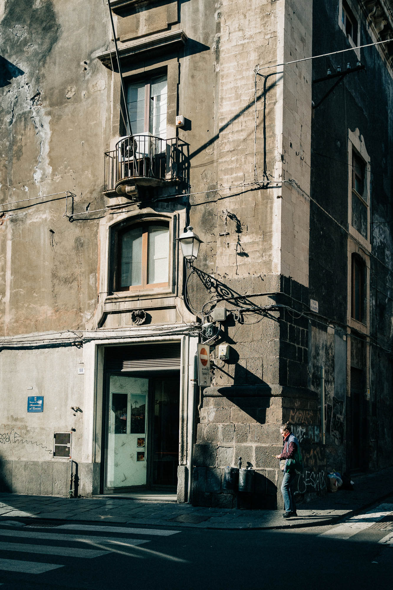 Street corner in Catania with harsh shadows and a person walking by