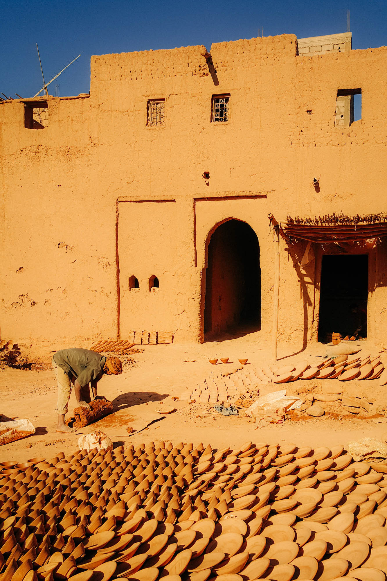 A man rolling clay at a traditional Moroccan pottery workshop among ceramics drying in the sun 