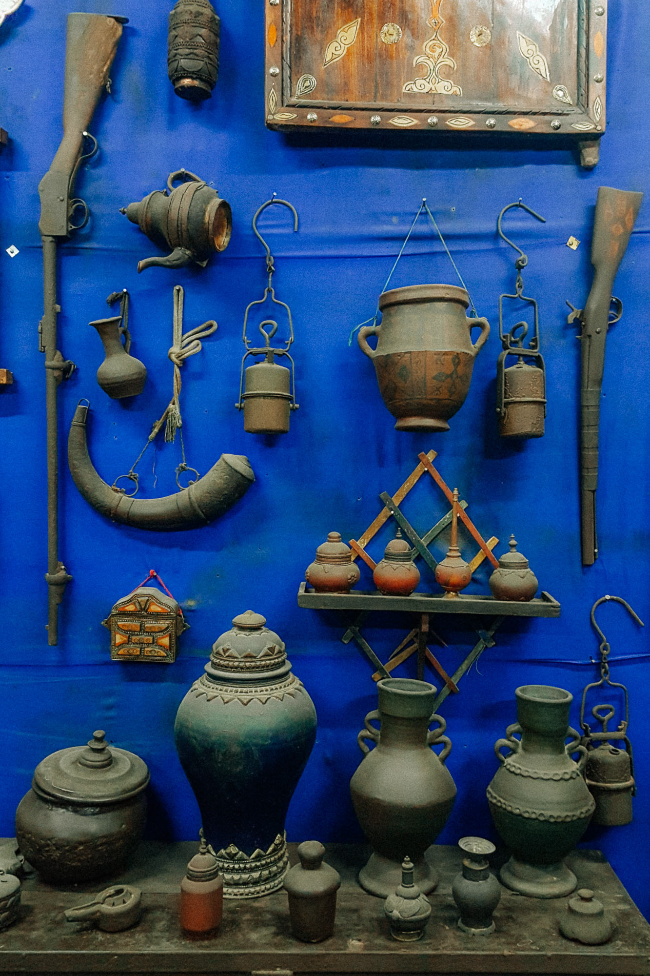 Antique Moroccan vases, pots, rifles and other paraphernalia placed in front of a royal blue wall