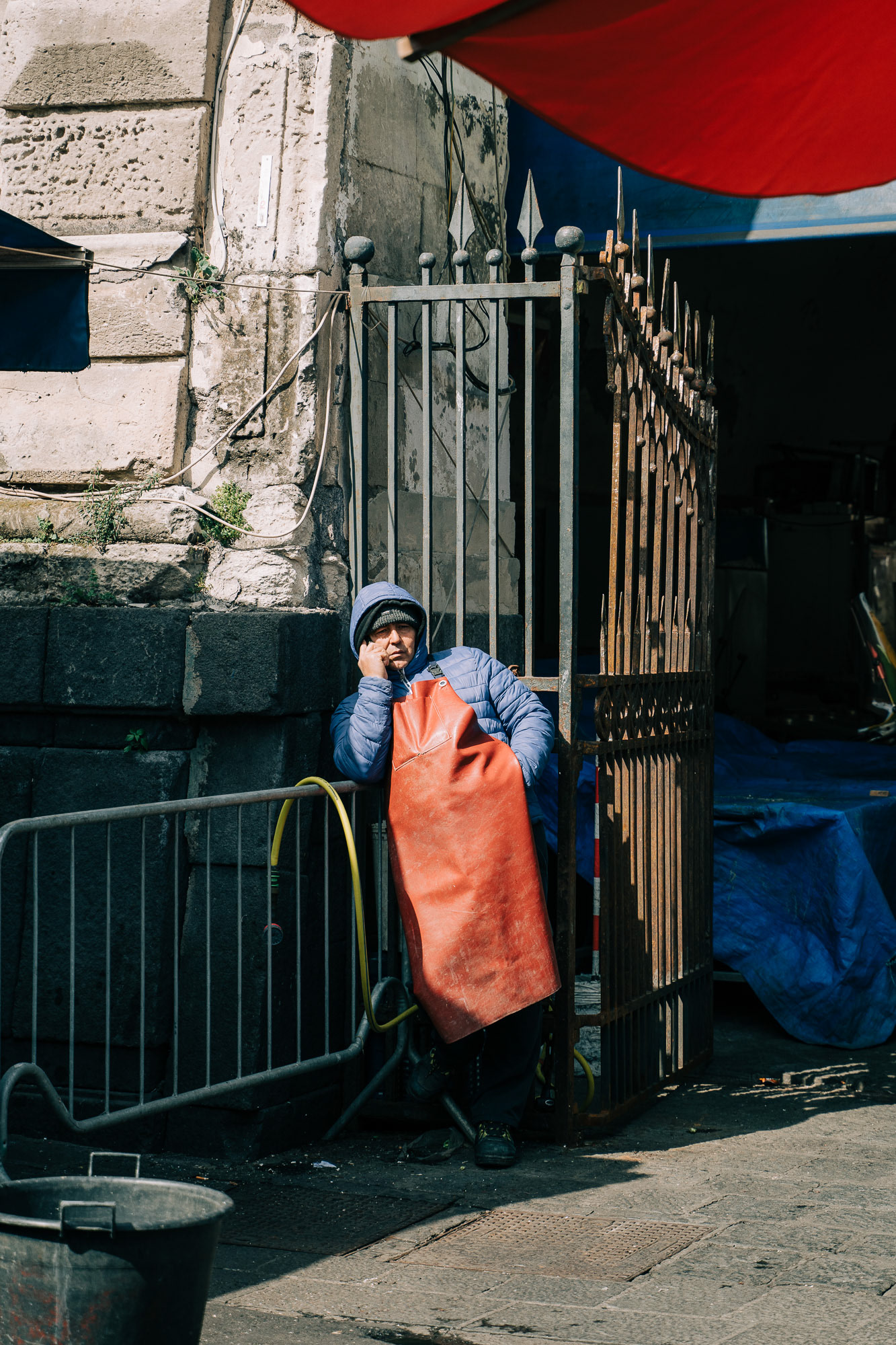 Street photography of a worker leaning on a gate at Catania's fish market