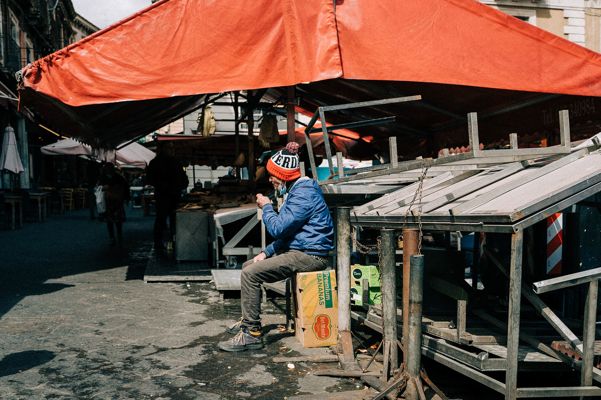 Street photgraphy showing a worker at La Pescheria dressed in red and blue sitting under a red umbrella