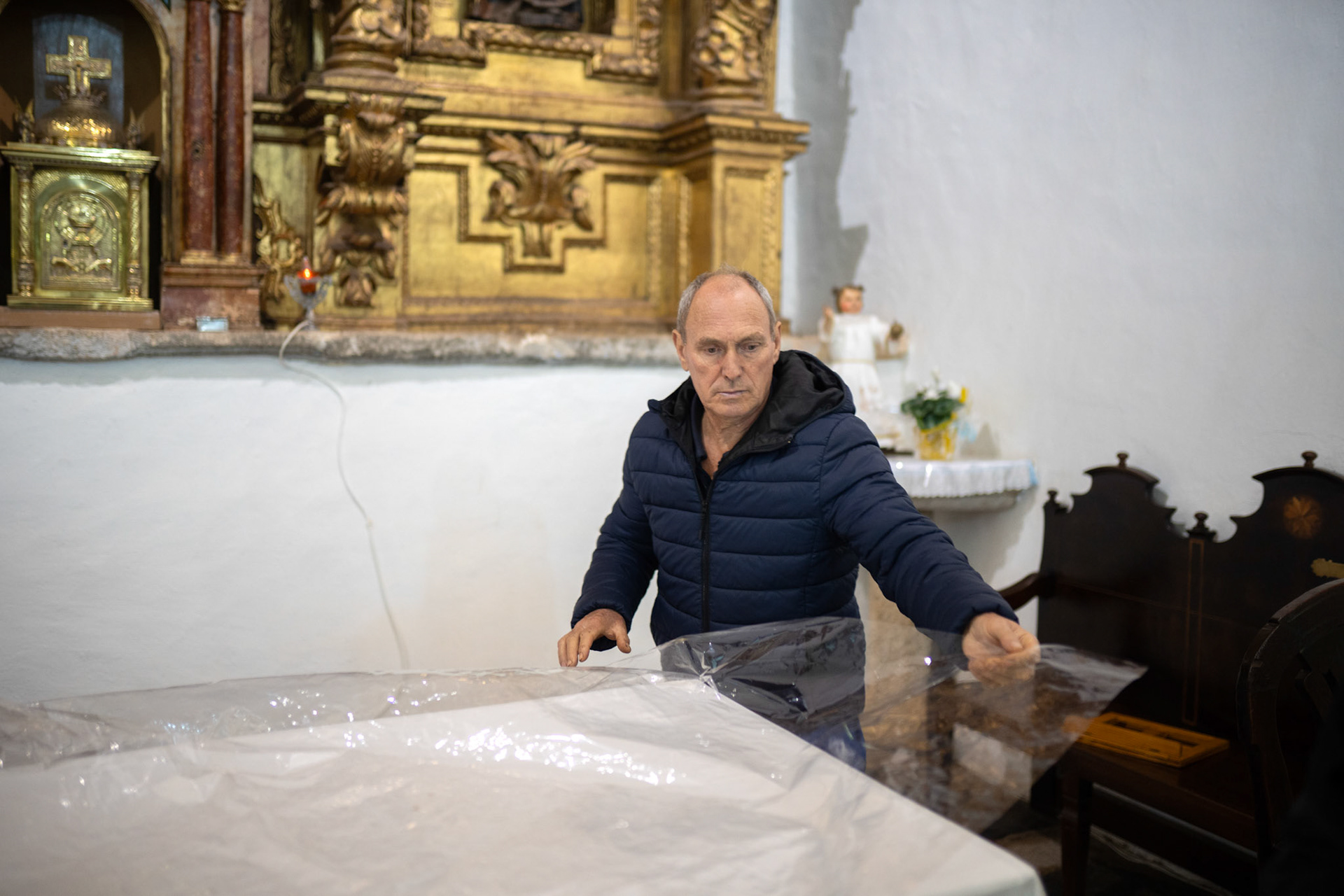 Un hombre coloca un plástico protector en el altar de la iglesia de Rabanales.