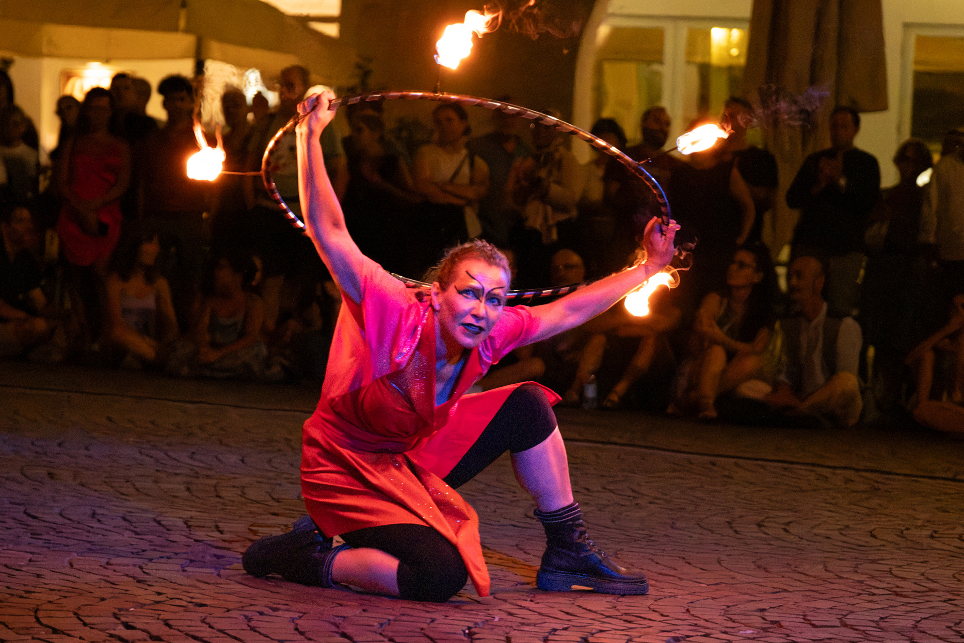 Una performer fa volteggiare un cerchio infuocato sopra la testa