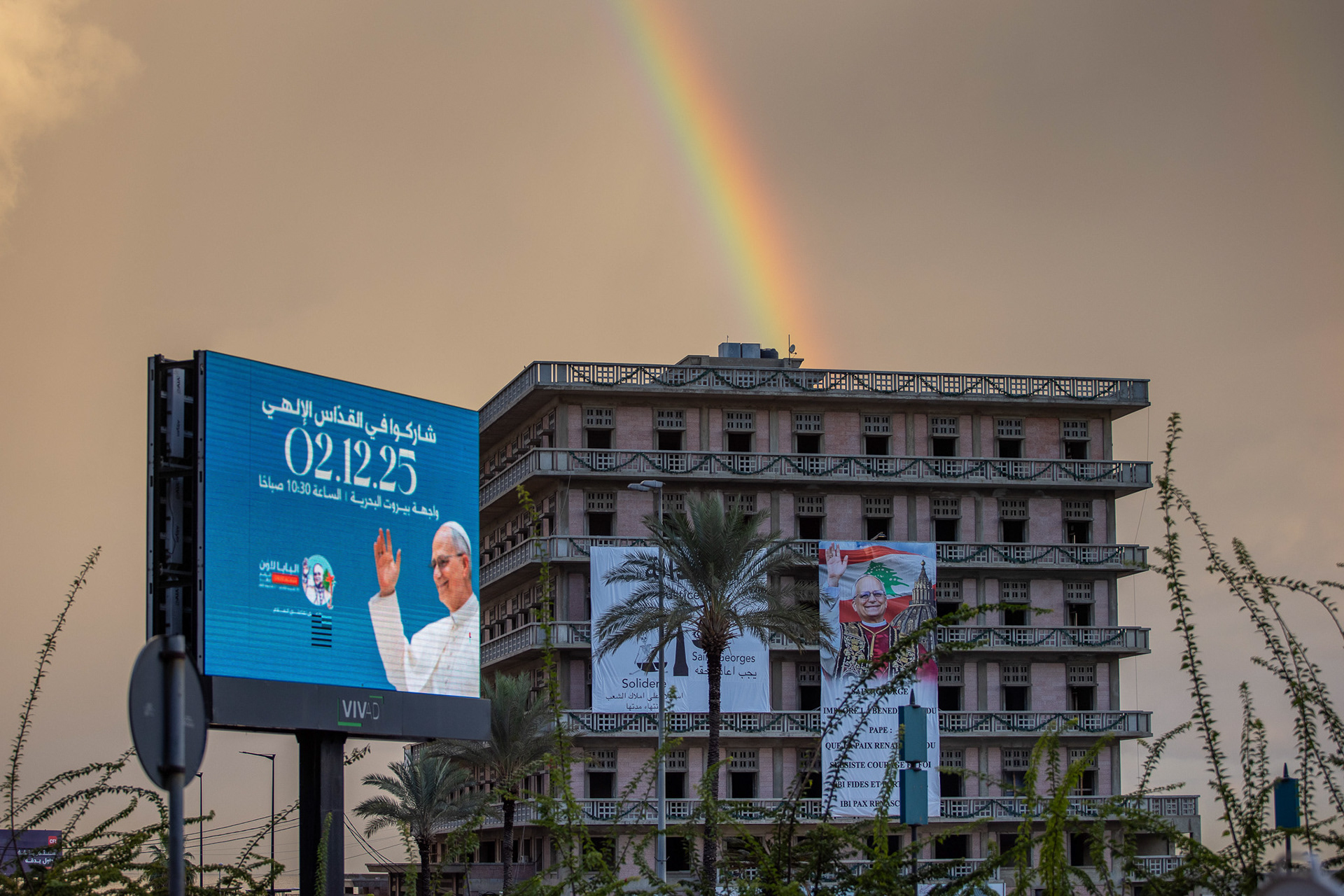 A banner depicting Pope Leo XIV against a morning rainbow before his visit to the Maronite Monastery in Annaya, Lebanon, where he will pray at the tomb of Saint Charbel. The rainbow symbolizes hope, peace, and unity in a diverse society. Photo by: © Marek Ladzinski/ZUMA Press Wire