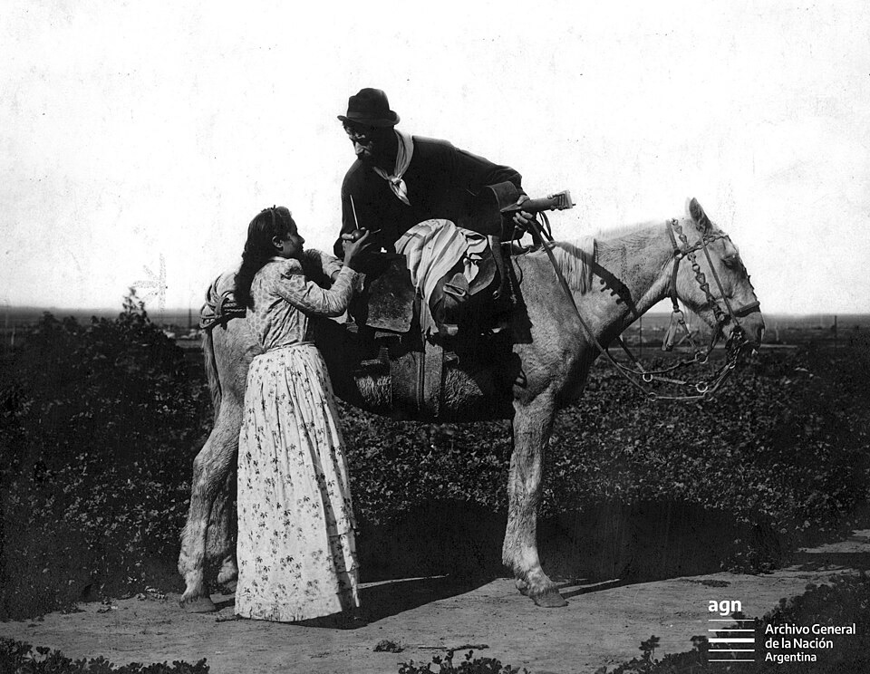 Un gaucho a cavallo condivide un mate mentre tiene la sua chitarra. Anno 1898.