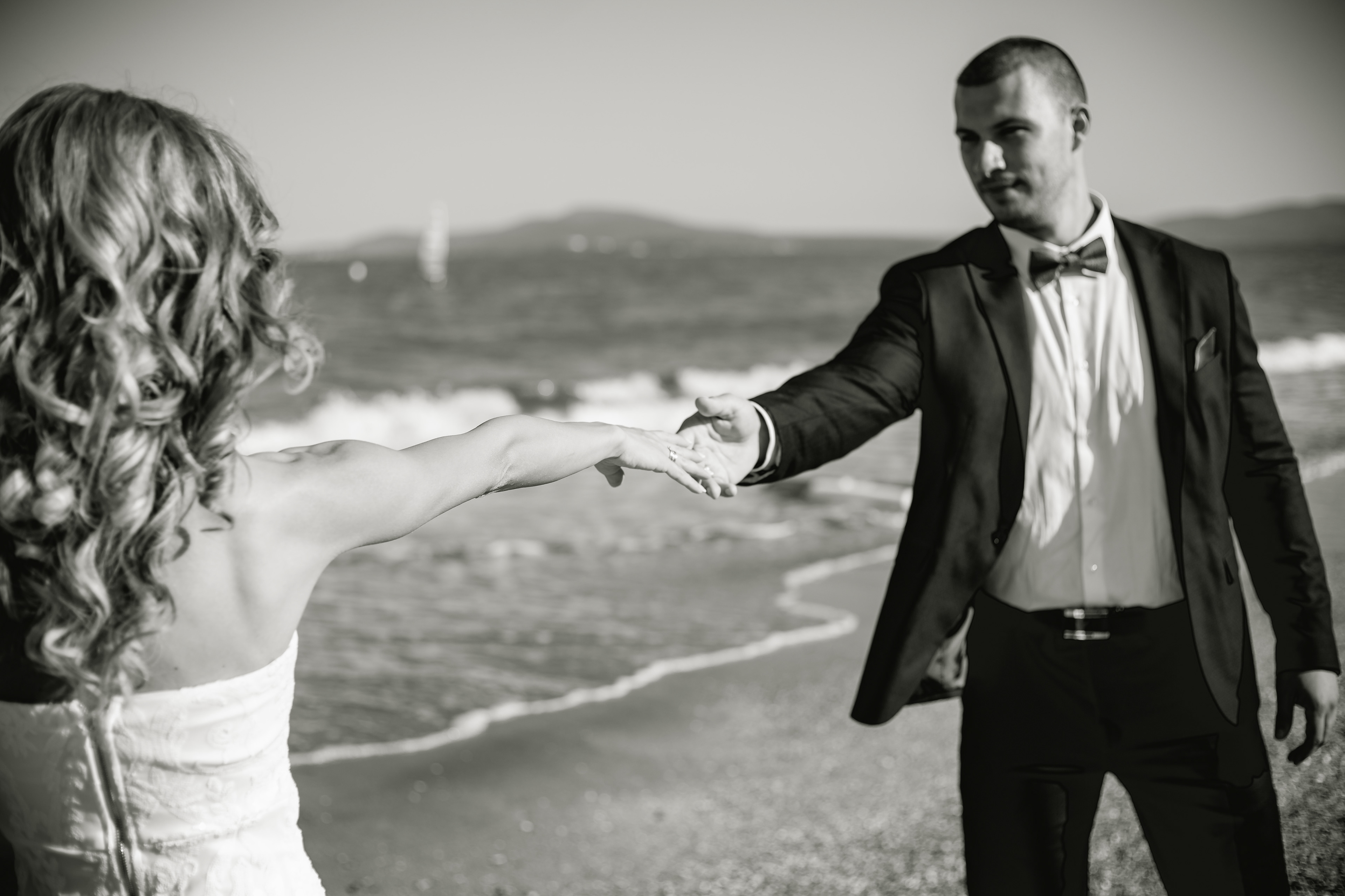 Черно-бяла сватбена фотография – младоженец и булка, хванати за ръце край морето, заснети от сватбен фотограф Габриел Александров