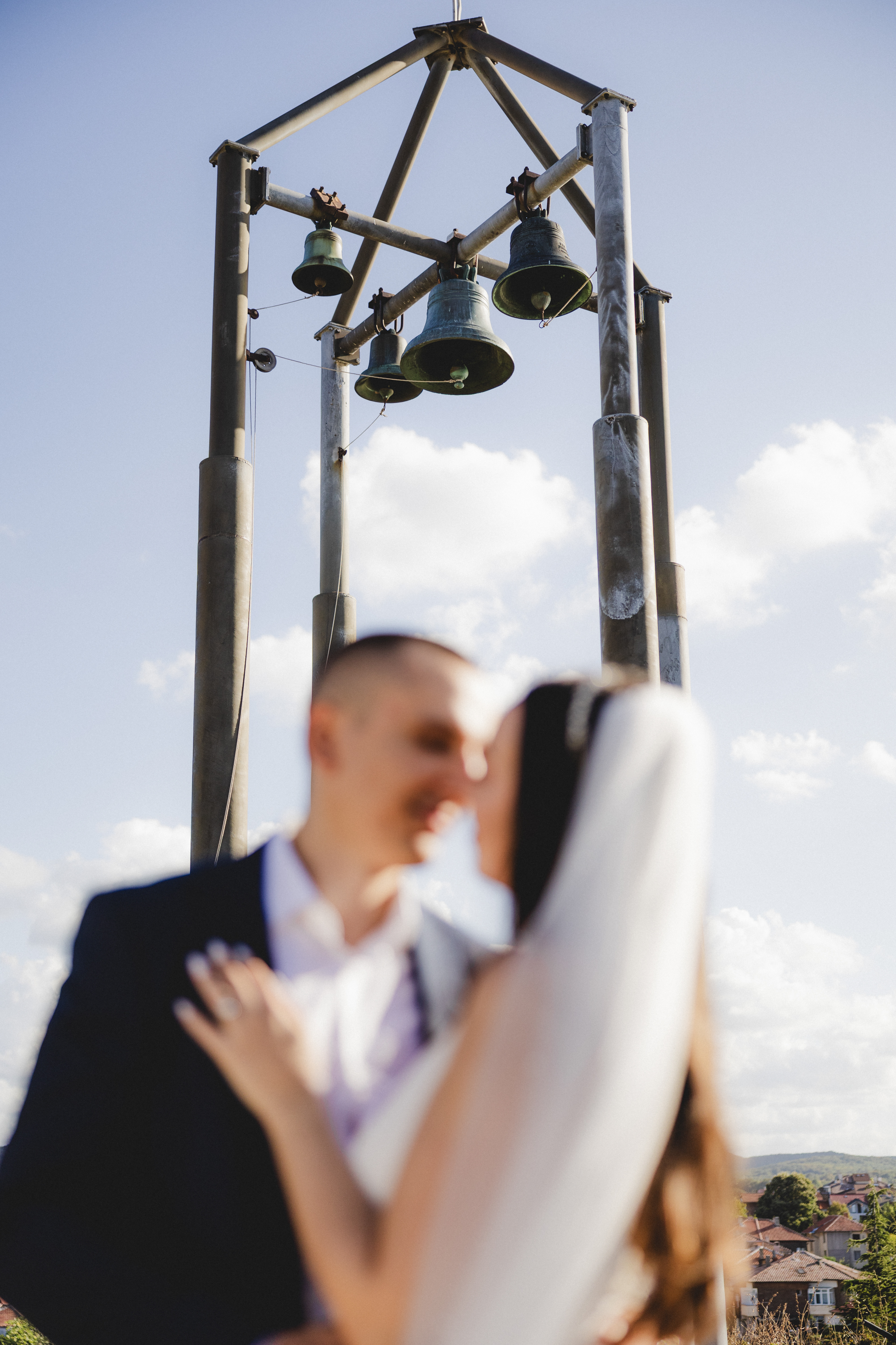 Младоженци нежно се докосват под камбаните на църквата Св. Успение Богородично в Царево – сватбен фотограф Габриел Александров