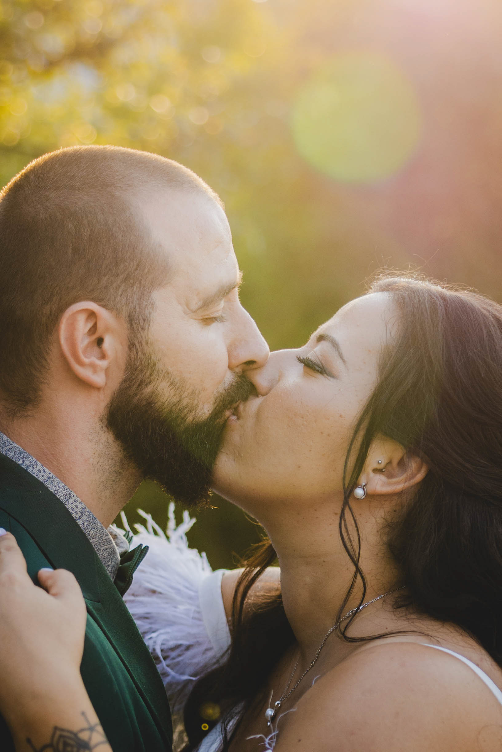 Целувка между младоженци в контражур, заснета от сватбен фотограф в парк Росенец