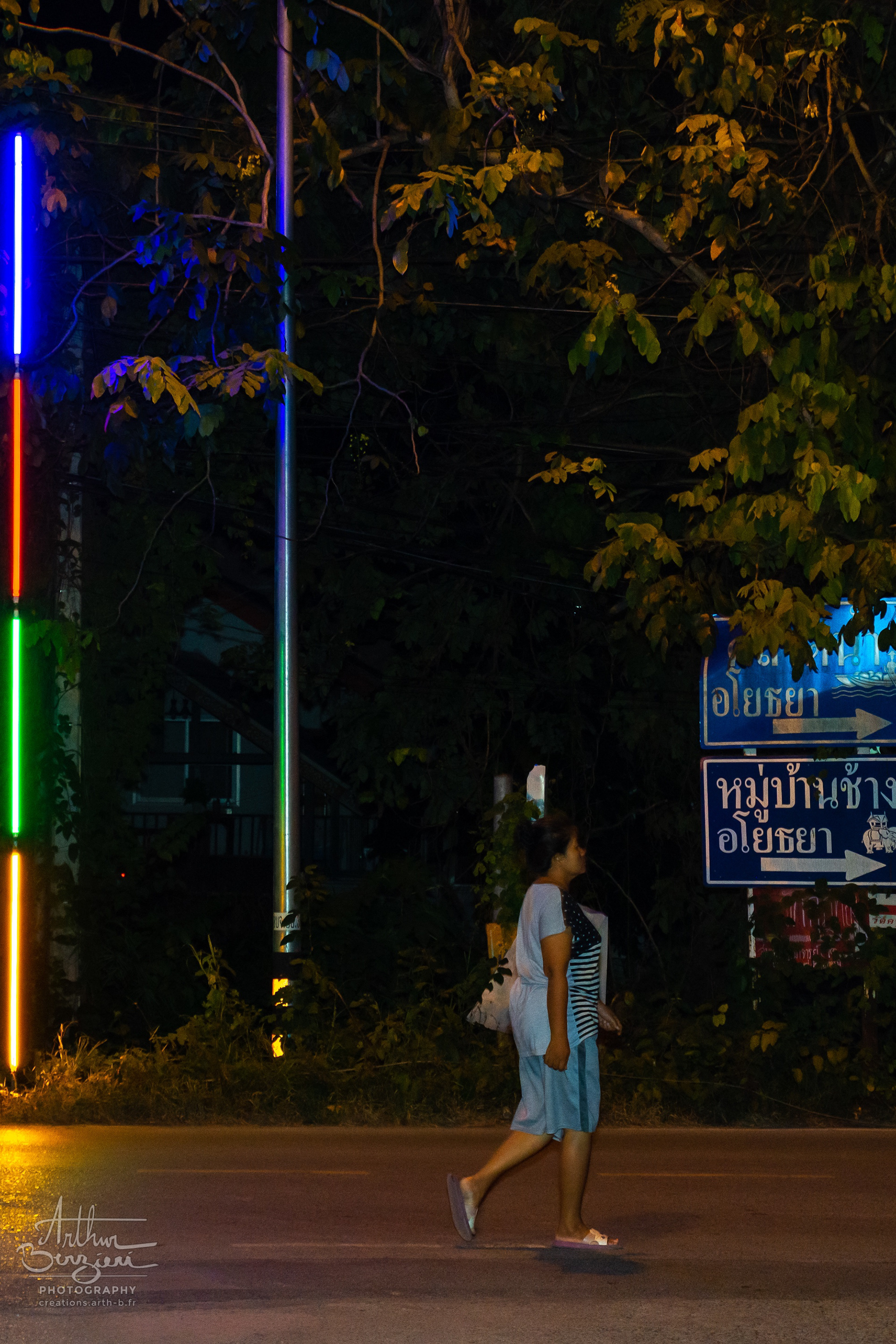 Par-là se dirige cette femme en pleine nuit, d'un pas décidé aux lueurs des scooters et luminaires colorés.