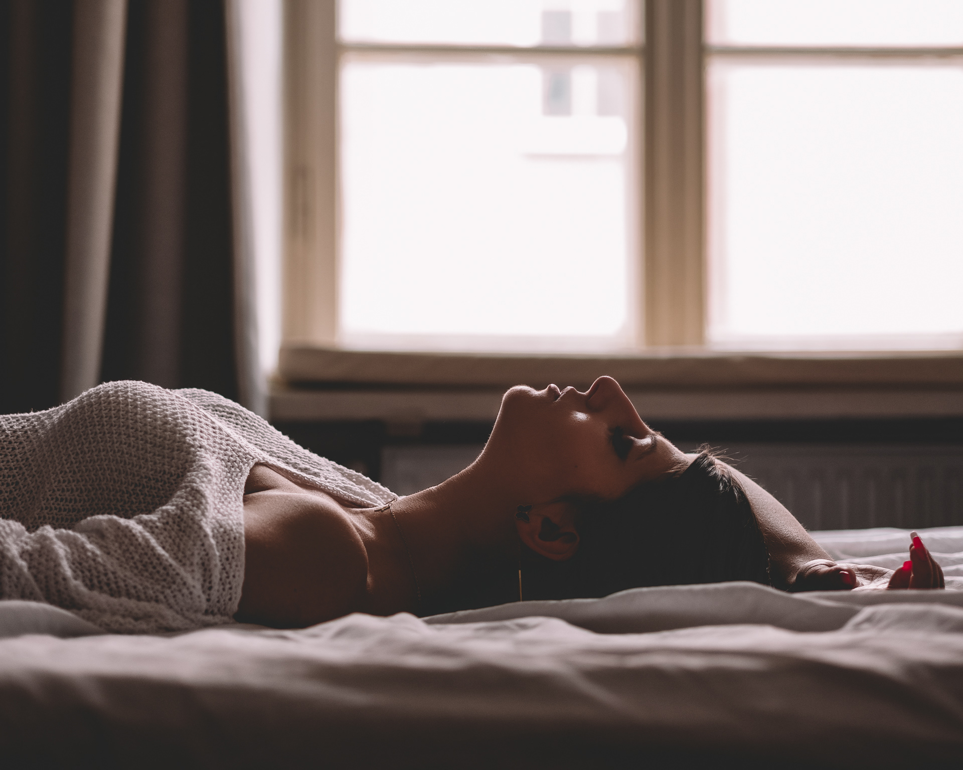 Sesja sensualna kobiety leżącej na łóżku na tle okna w apartamencie w Warszawie. Fotograf Warszawa
