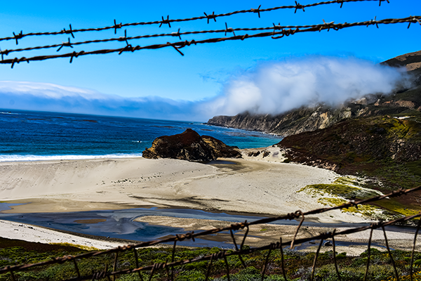 Coastal landscape photograph using barbed wire as a foreground framing element to contrast rugged shoreline with dramatic cloud cover.