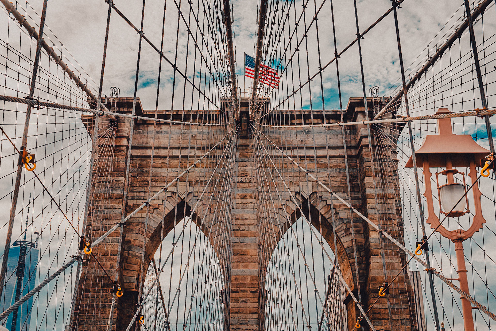 (EN) The Brooklyn Bridge is a bridge in New York City and is one of the oldest suspension bridges in the United States. Completed in 1883, it connects the boroughs of Manhattan and Brooklyn by spanning the East River. It has a main span of 1,595.5 feet, and was the first steel-wire suspension bridge constructed. Since its opening, it has become an icon of New York City, and was designated a National Historic Landmark in 1964 and a National Historic Civil Engineering Landmark in 1972.(ES) El puente de Brooklyn es un puente en la ciudad de Nueva York y es uno de los puentes colgantes más viejos de los Estados Unidos. Terminado en 1883, conecta las ciudades de Manhattan y de Brooklyn atravesando el East River. Tiene un palmo principal de 486,3 metros, y fue el primer puente colgante de alambre de acero. Desde su apertura, se ha convertido en un icono de la ciudad de Nueva York, y fue designado Monumento Histórico Nacional en 1964 y un Monumento Histórico Nacional de Ingeniería Civil en 1972.