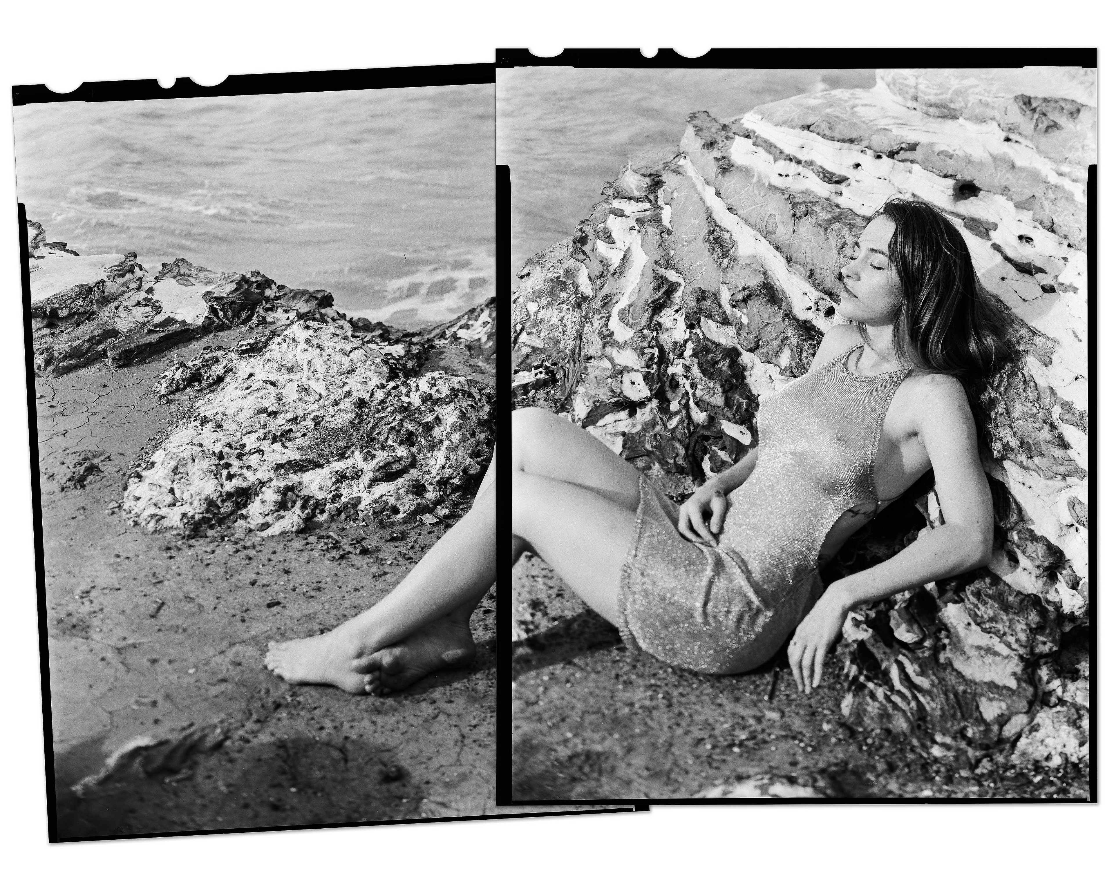 Woman laying on rocks beside a beach in a dress