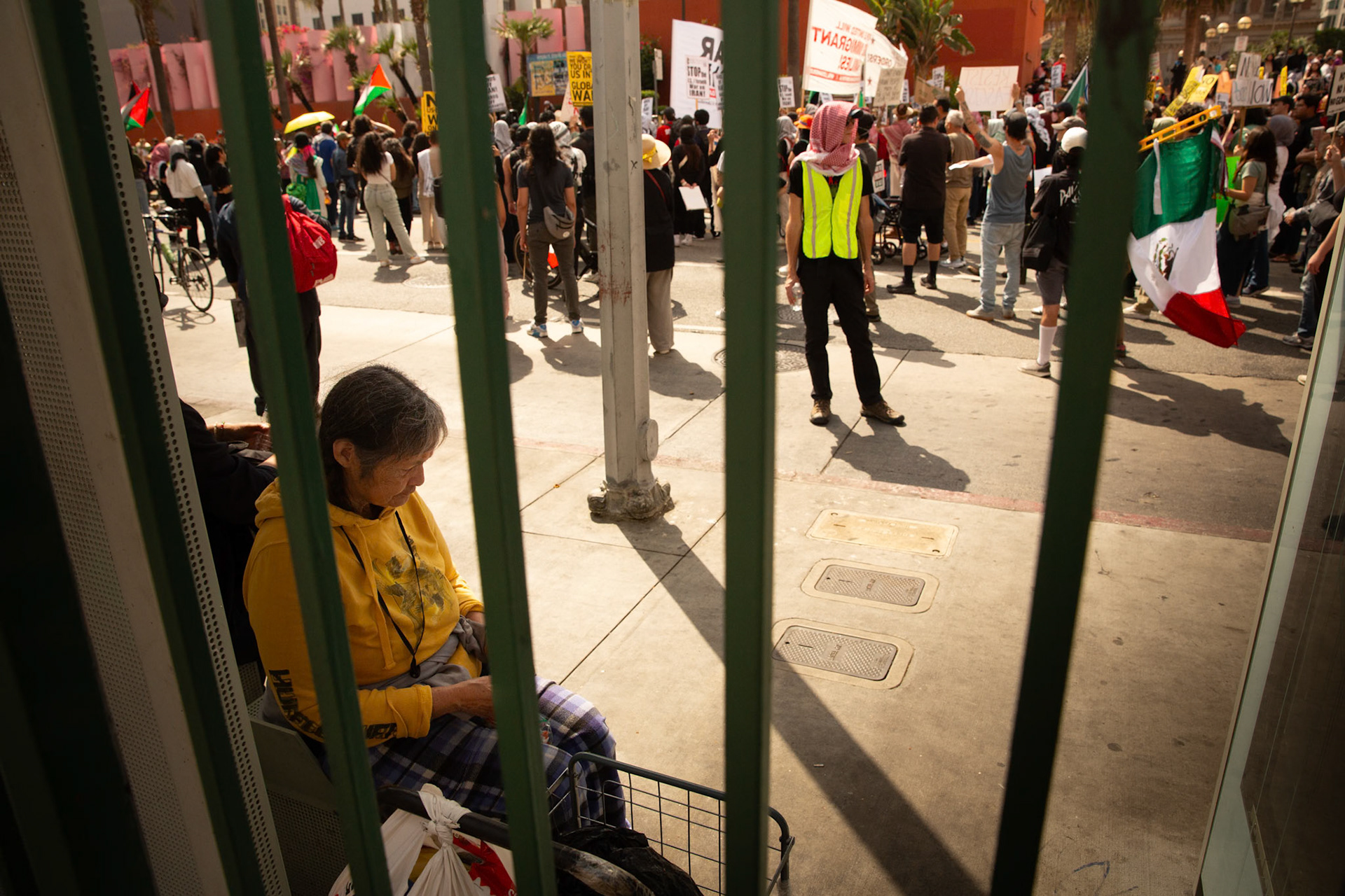 A commuter waits for the bus as demonstrators gather at Pershing Square in Los Angeles Calif. on June 21, 2025 during a demonstration against U.S. involvement in the war between Israel and Iran.