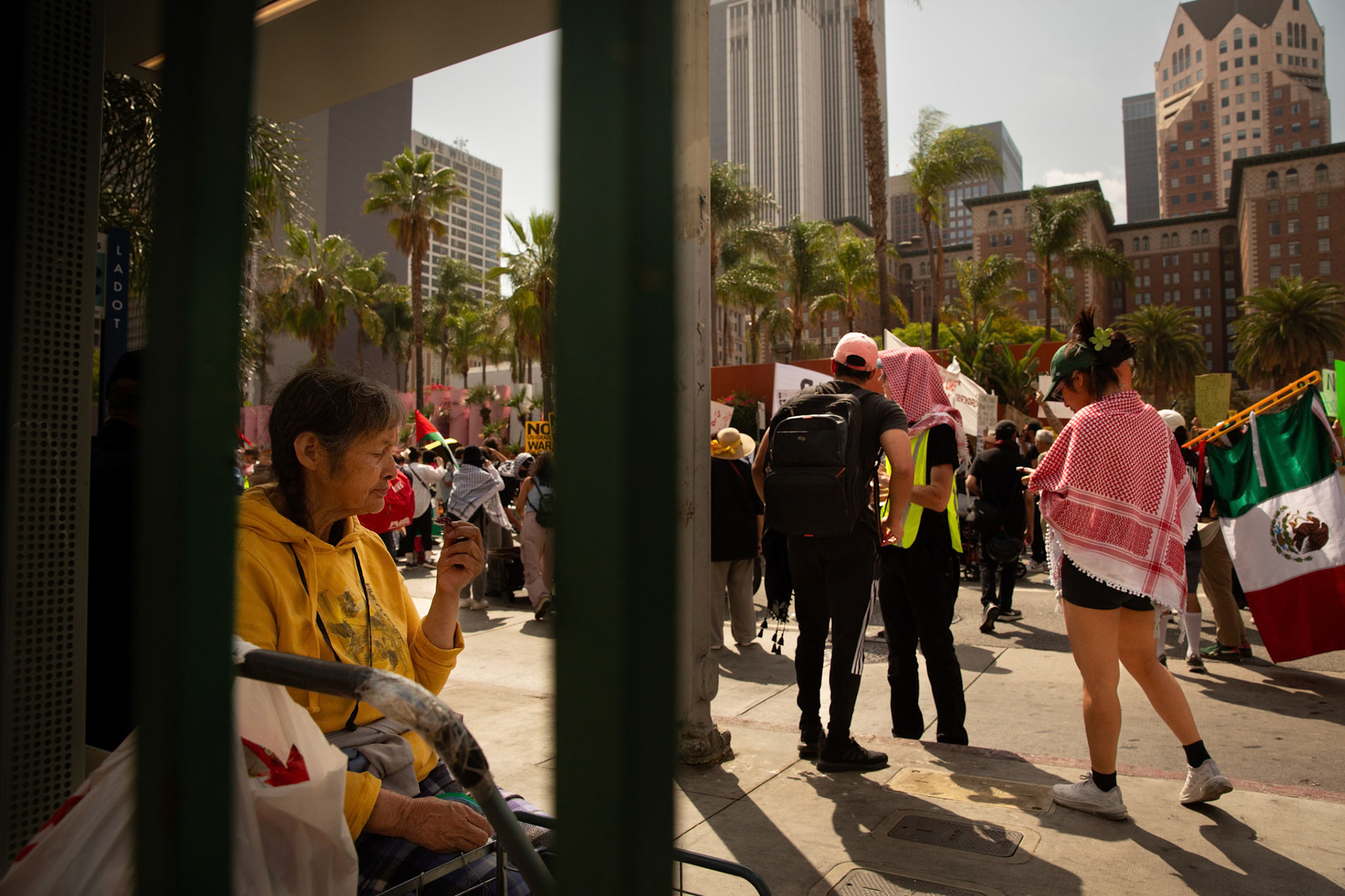 A commuter waits for the bus as demonstrators gather at Pershing Square in Los Angeles Calif. on June 21, 2025 during a demonstration against U.S. involvement in the war between Israel and Iran.
