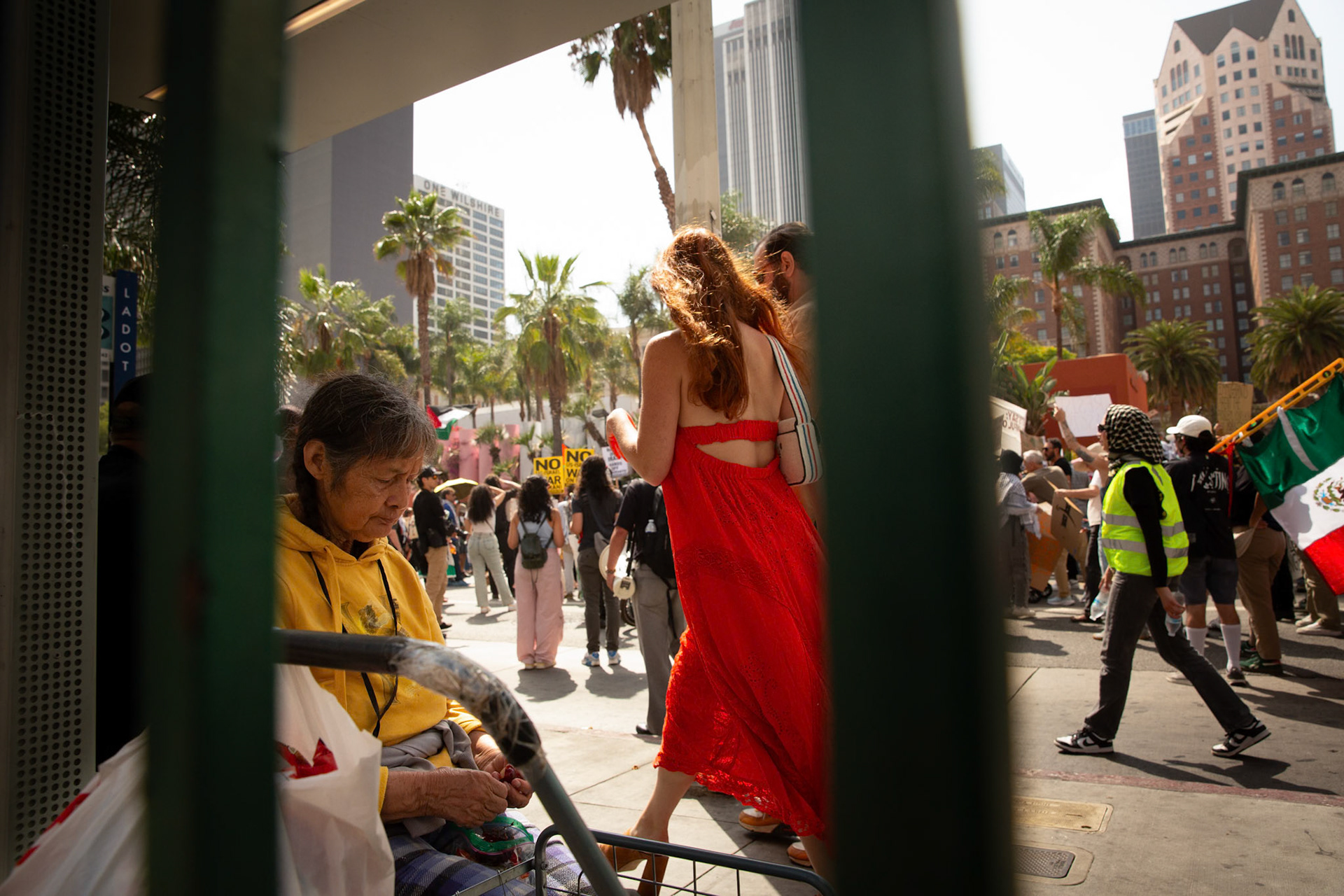 A commuter waits for the bus as demonstrators gather at Pershing Square in Los Angeles Calif. on June 21, 2025 during a demonstration against U.S. involvement in the war between Israel and Iran.