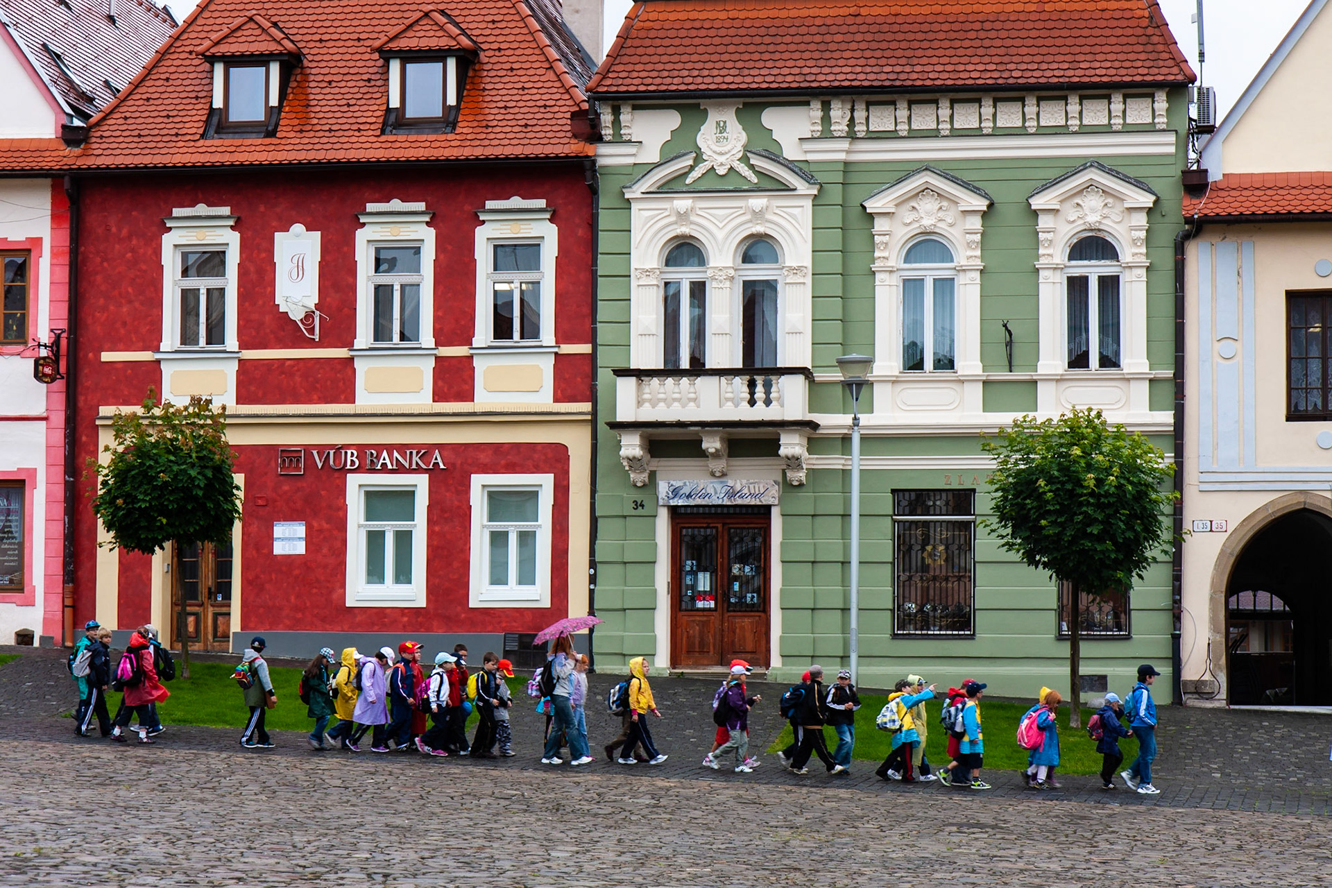 Children march, all in a row, through the rain.