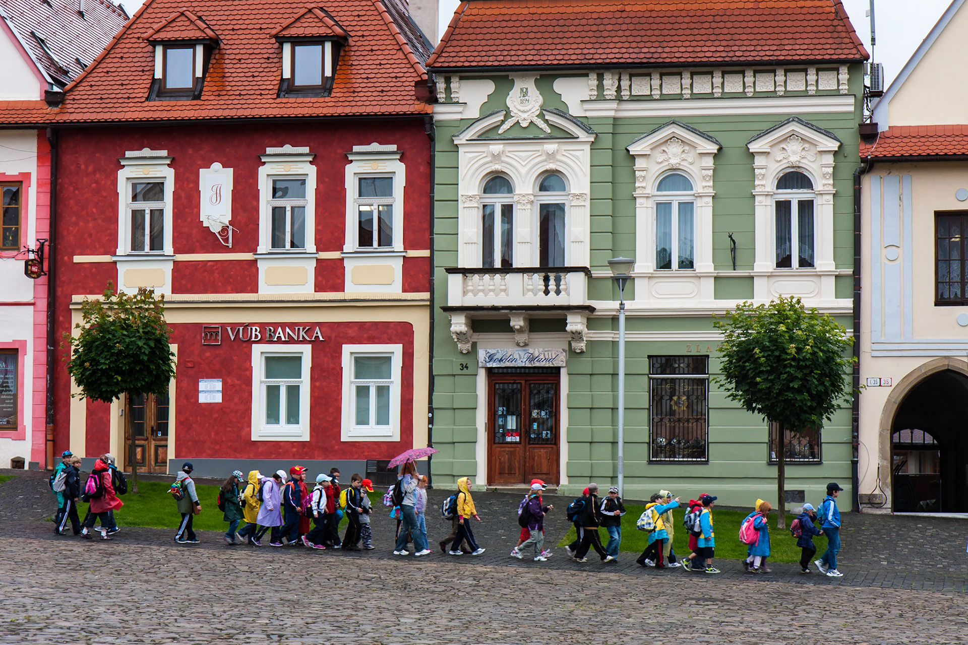 Children march, all in a row, through the rain.