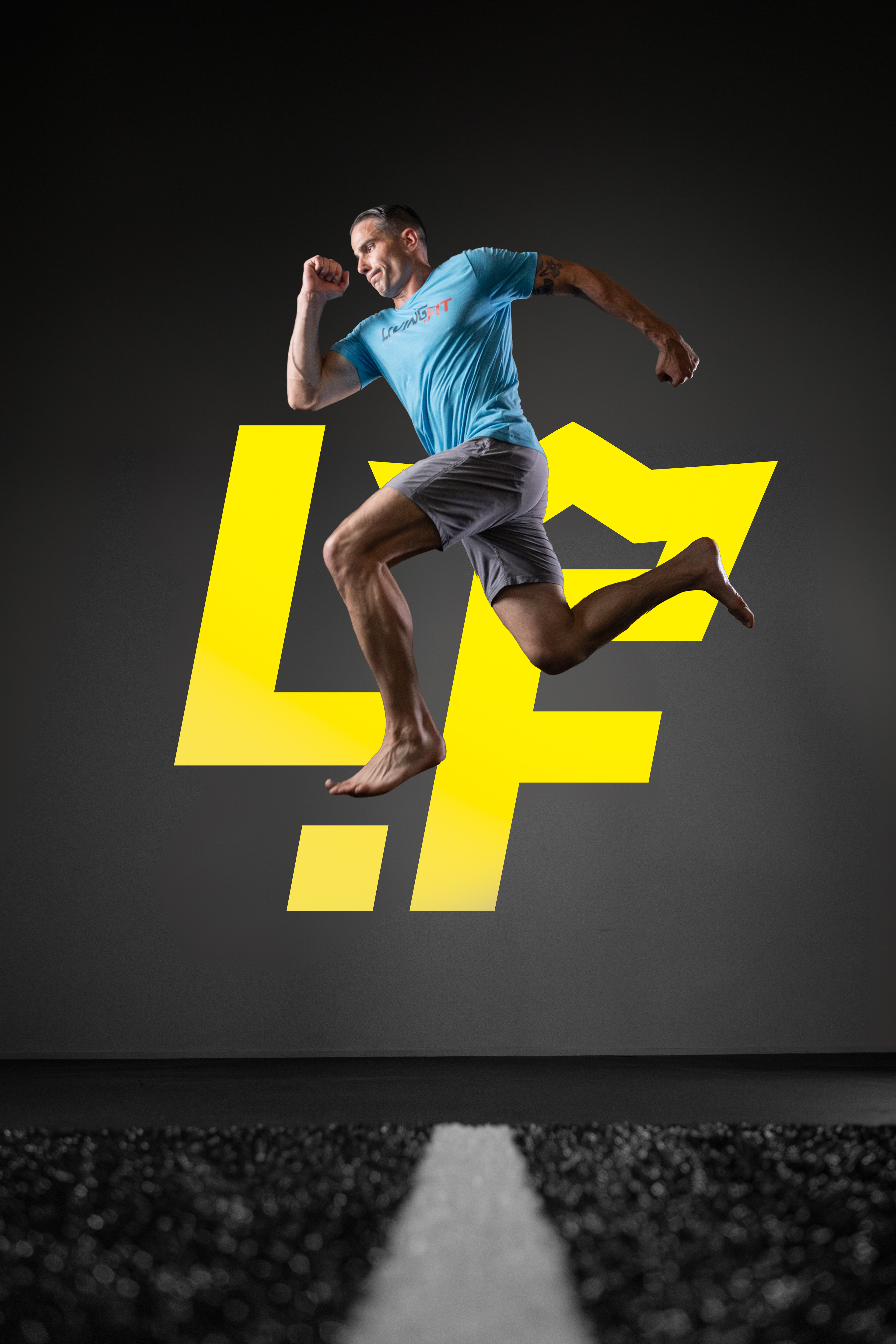 The image depicts a man mid-jump against a dark background, with a large yellow stylized crown logo behind him. He is wearing a light blue T-shirt with the text "Living Fit" and gray shorts. The man appears to be in motion, suggesting an active or fitness-related theme.