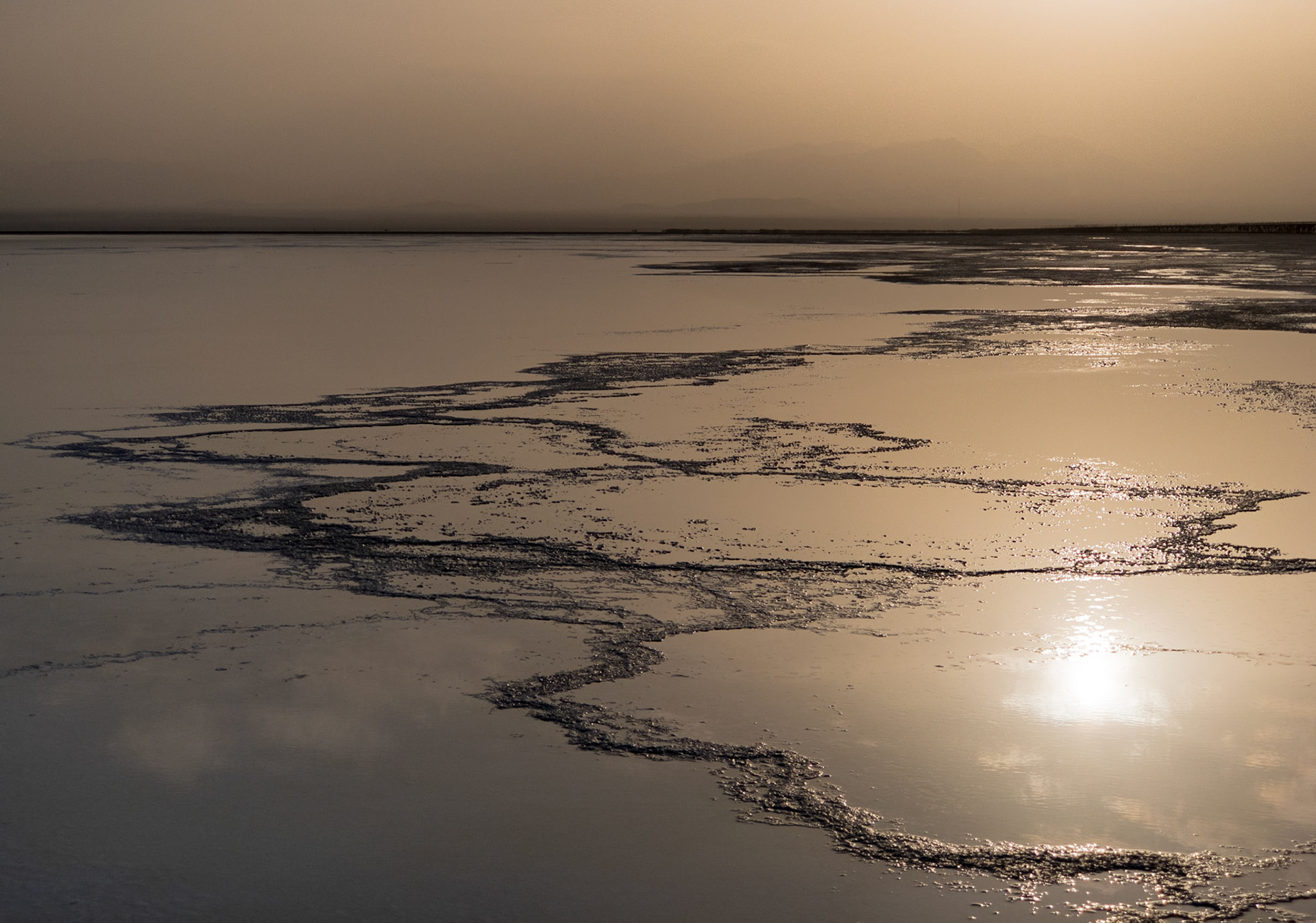 Ridges of salt stand out in silhouette against the warm,  mirrored image of sunset at Lake Asale in Ethiopia's hot, dry Danakil Depression, the most inhospitable place on Earth.