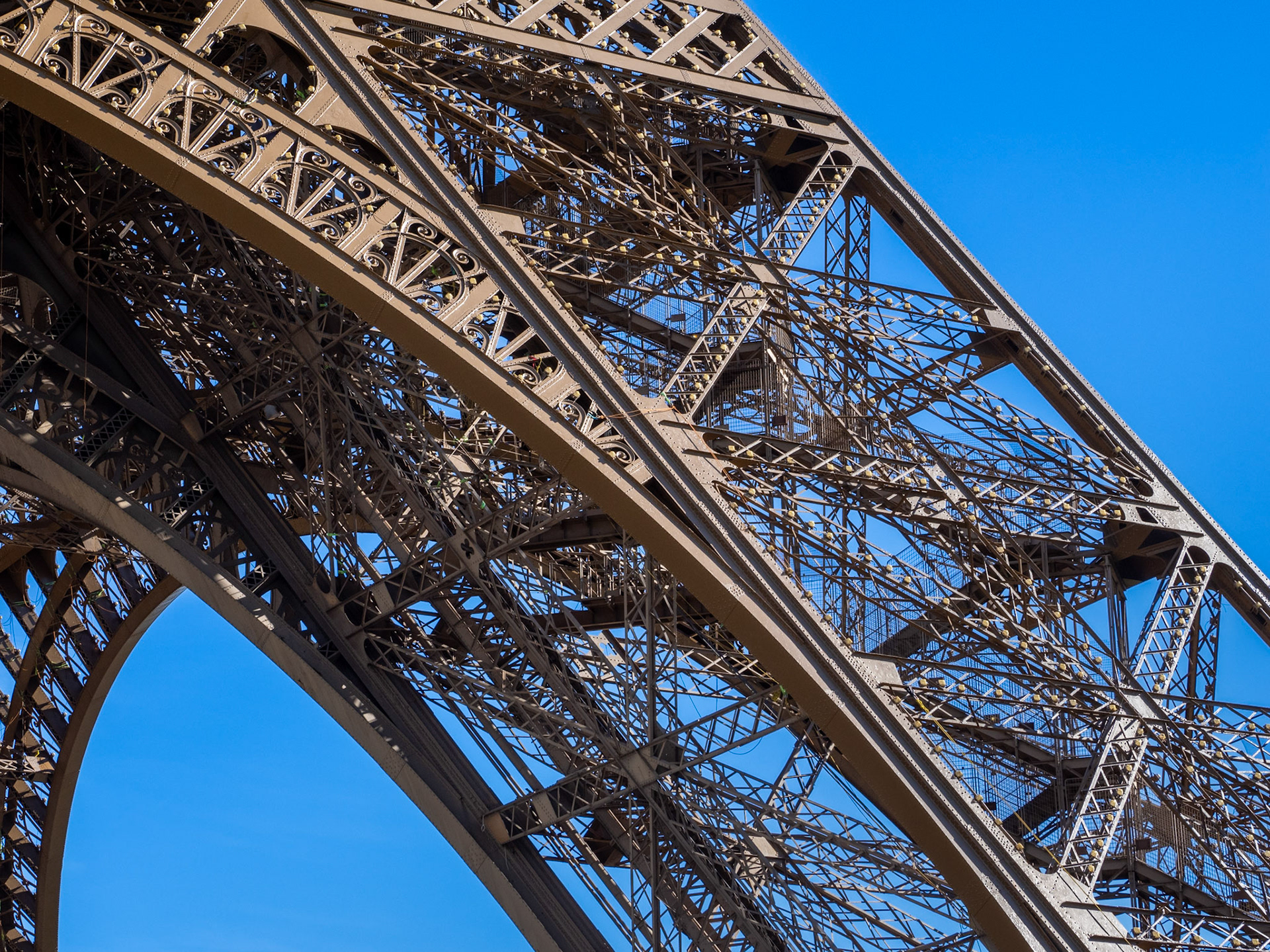A close-up of the patterns created by the iron work on one leg of the Eiffel Tower, Paris, set against a vivid, clear blue sky