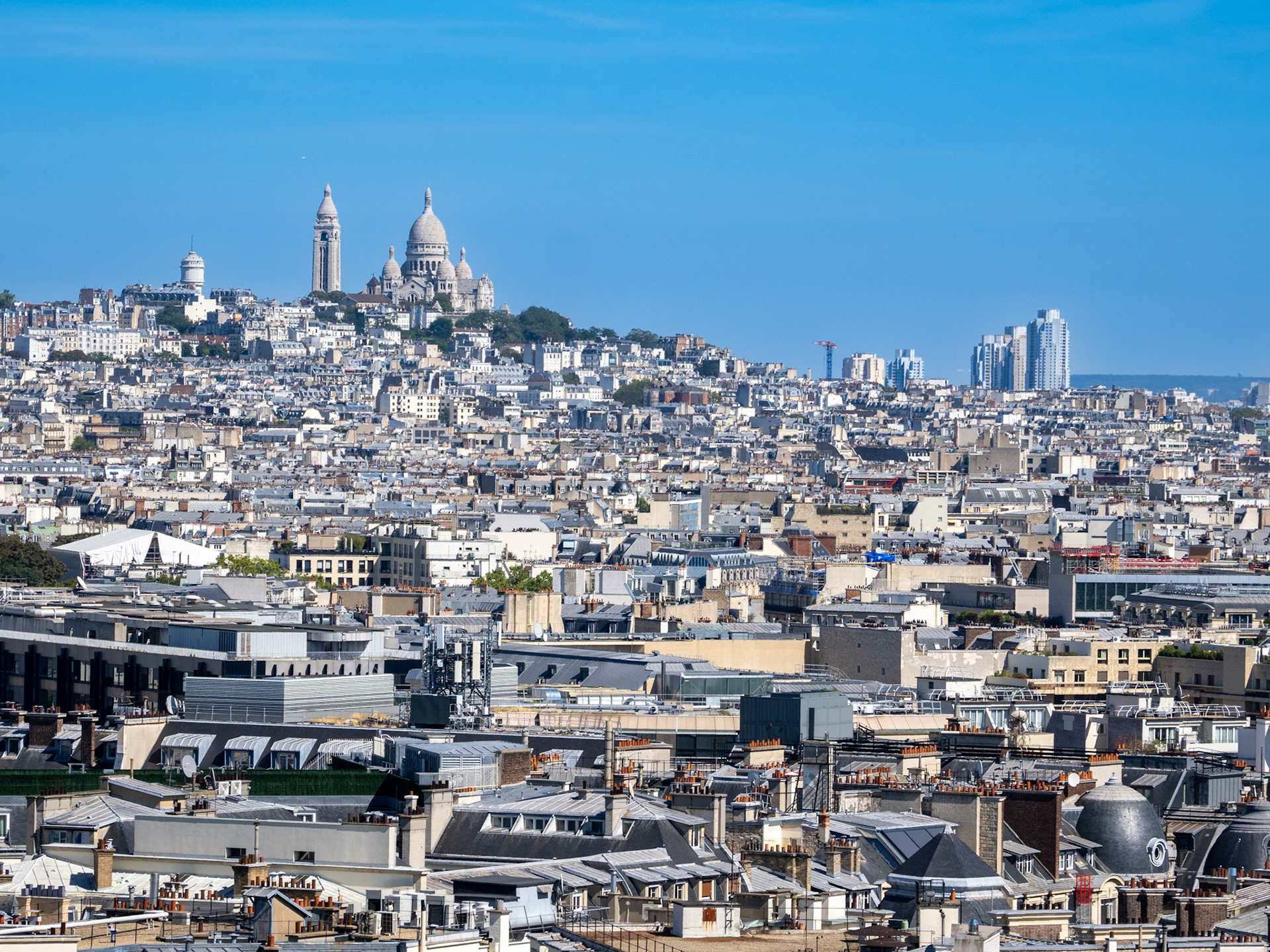 The bright white apartments of the city of Paris fill the space in this compressed, telephoto view of the hill of Montmartre and Sacré-Cœur Basilica skyline as seen from the Arc de Triomphe.